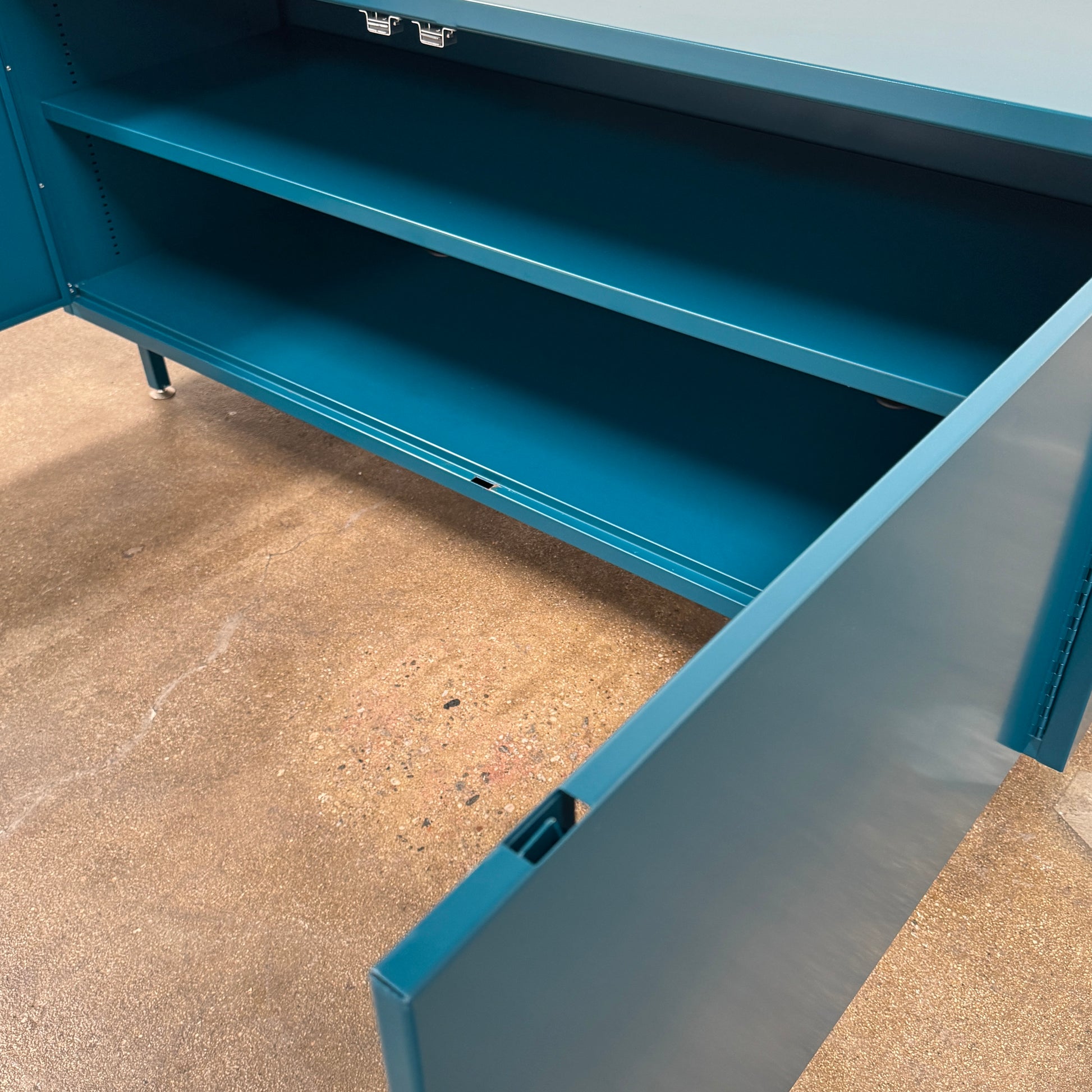 A blue metal Heartwork Active Duty Storage Credenza with two doors, a central lock, and four legs stands against a plain white background—this Heartwork piece offers durable construction ideal for workplace storage.