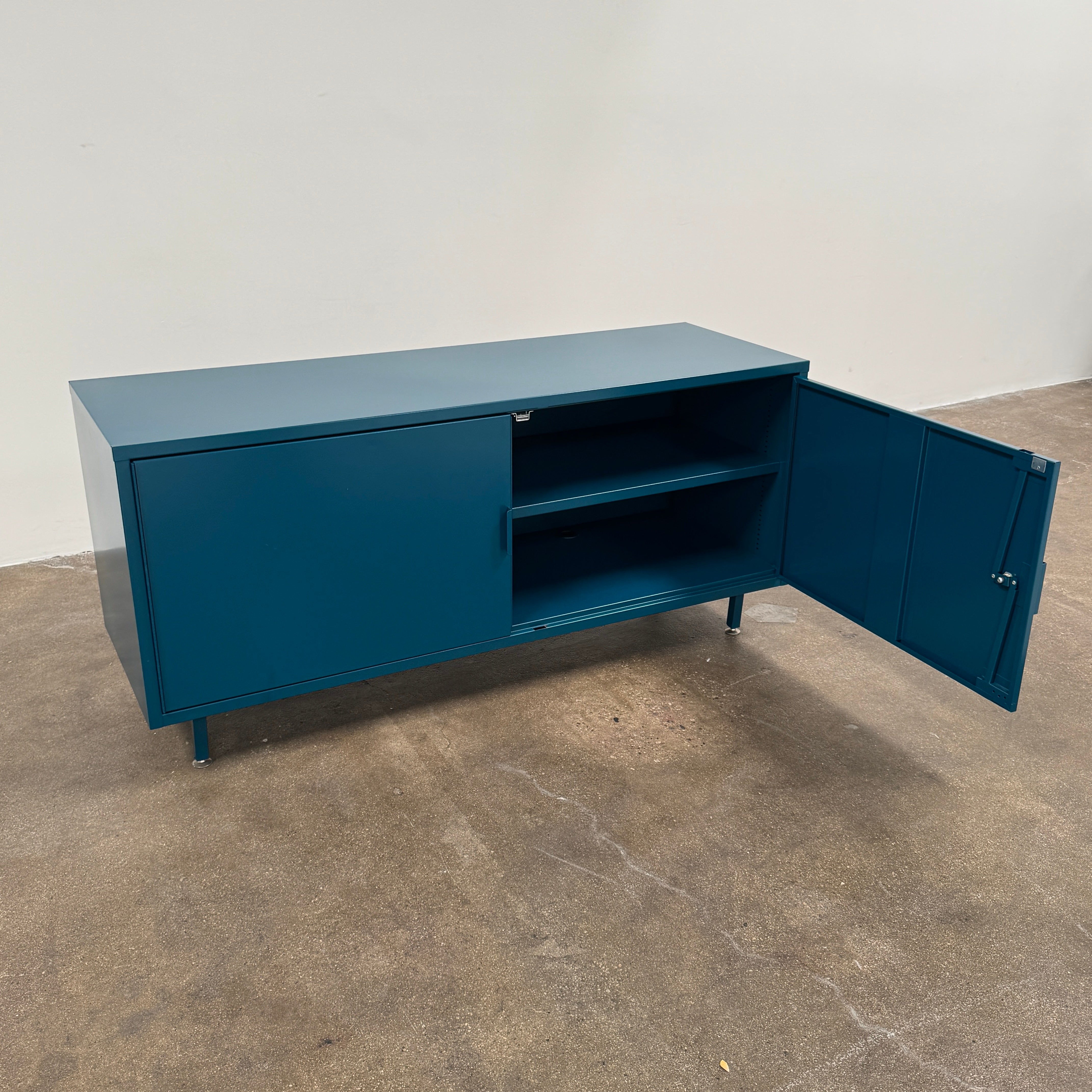 A blue metal Heartwork Active Duty Storage Credenza with two doors, a central lock, and four legs stands against a plain white background—this Heartwork piece offers durable construction ideal for workplace storage.