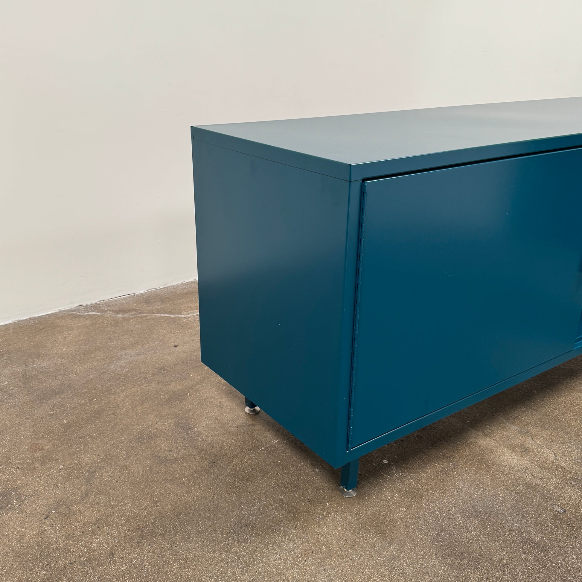 A blue metal Heartwork Active Duty Storage Credenza with two doors, a central lock, and four legs stands against a plain white background—this Heartwork piece offers durable construction ideal for workplace storage.