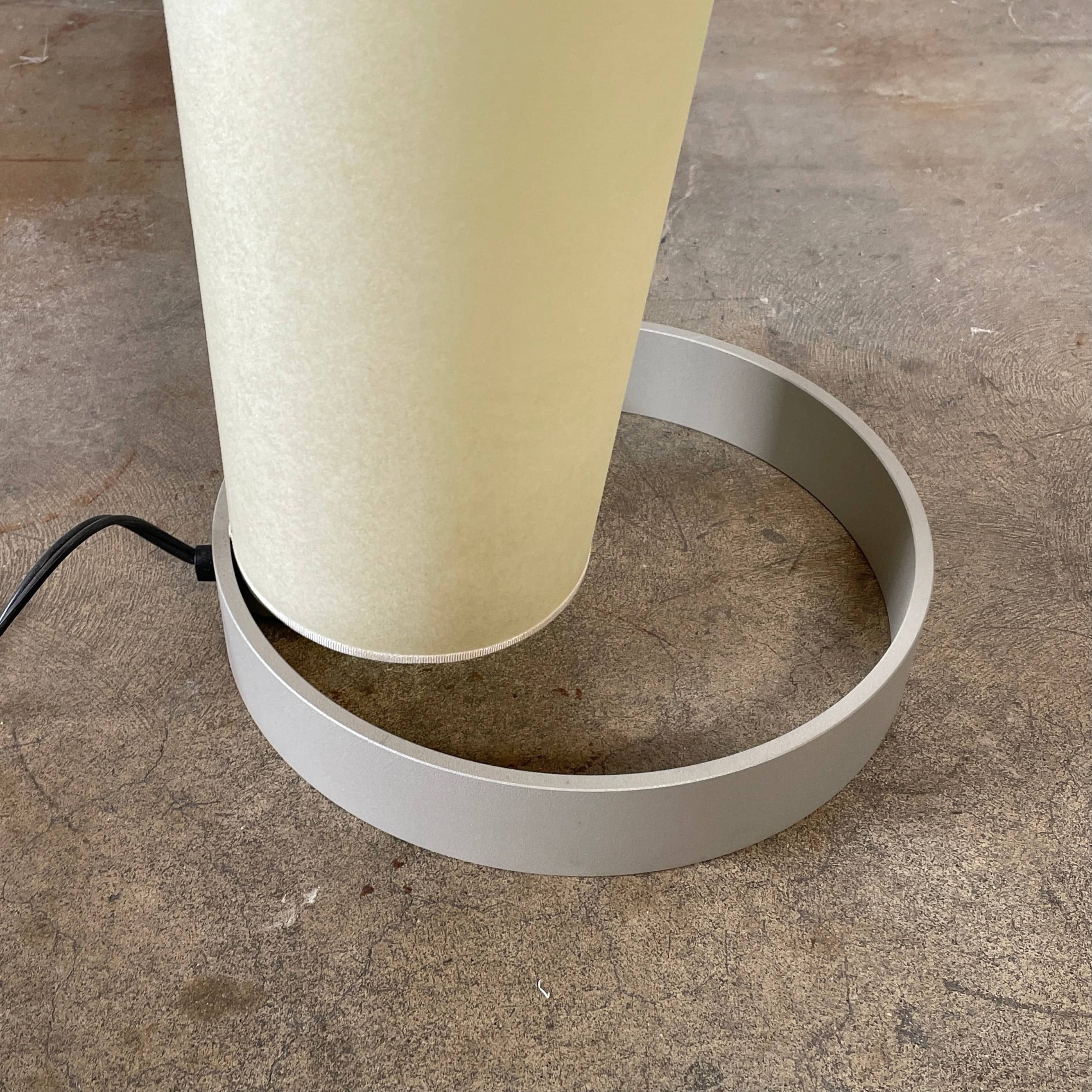 A modern, cone-shaped beige Pallucco Italia Abat Jour Floor Light by Pallucco Italia features a round base and a visible power cord, blending sleek design with Italian craftsmanship.