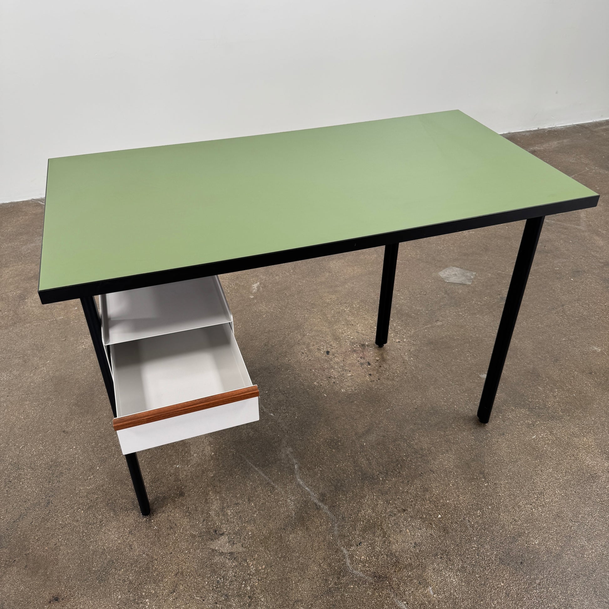 The Herman Miller Mode Desk by Herman Miller features a rectangular green tabletop, black legs, and three white drawers mounted underneath the left side—perfect as a compact desk for a minimalist workspace.