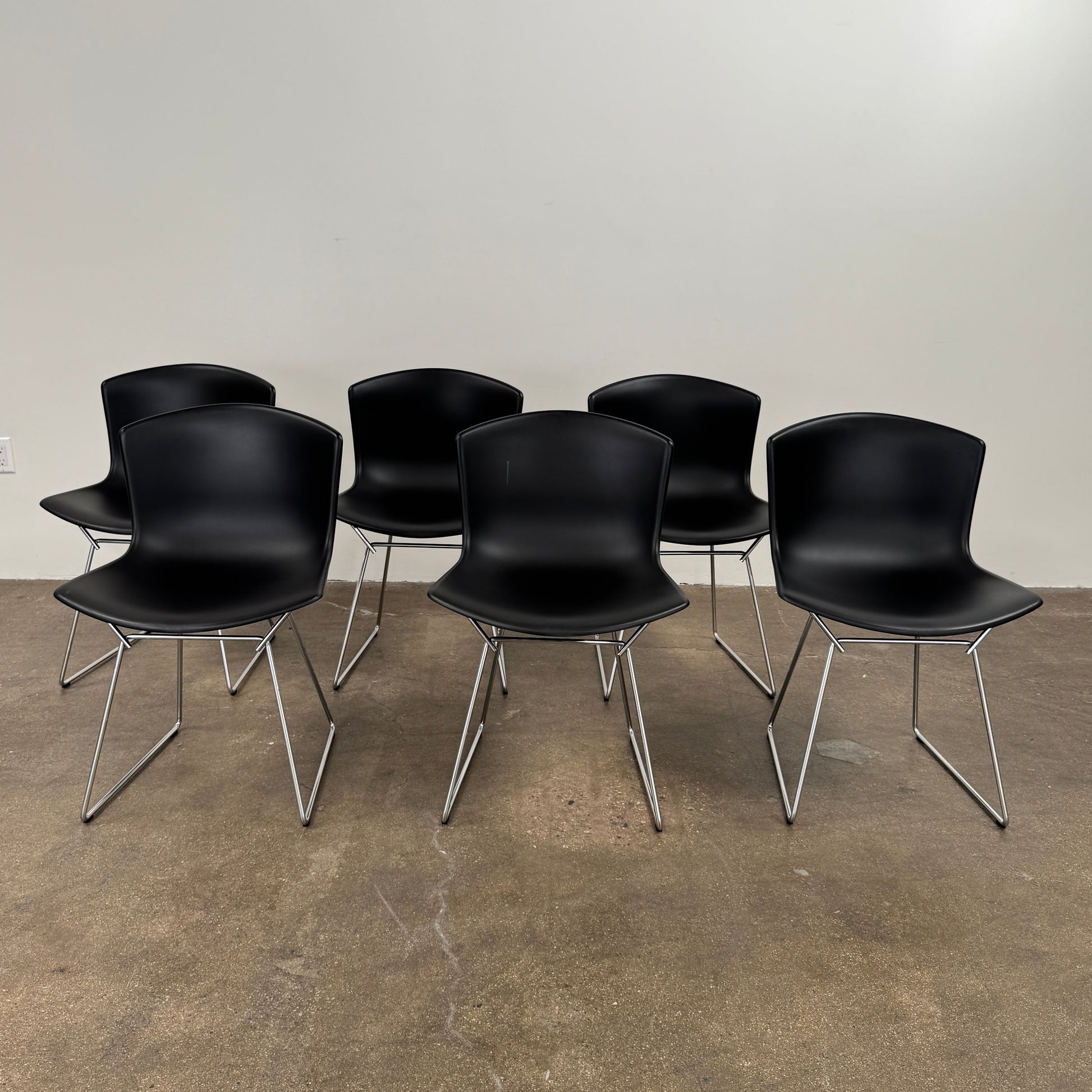 Eight Knoll Bertoia Molded Shell Chairs by Knoll, featuring black plastic seats and metal legs, are arranged in two rows on a white background, showcasing the sleek, timeless silhouette inspired by mid-century design.