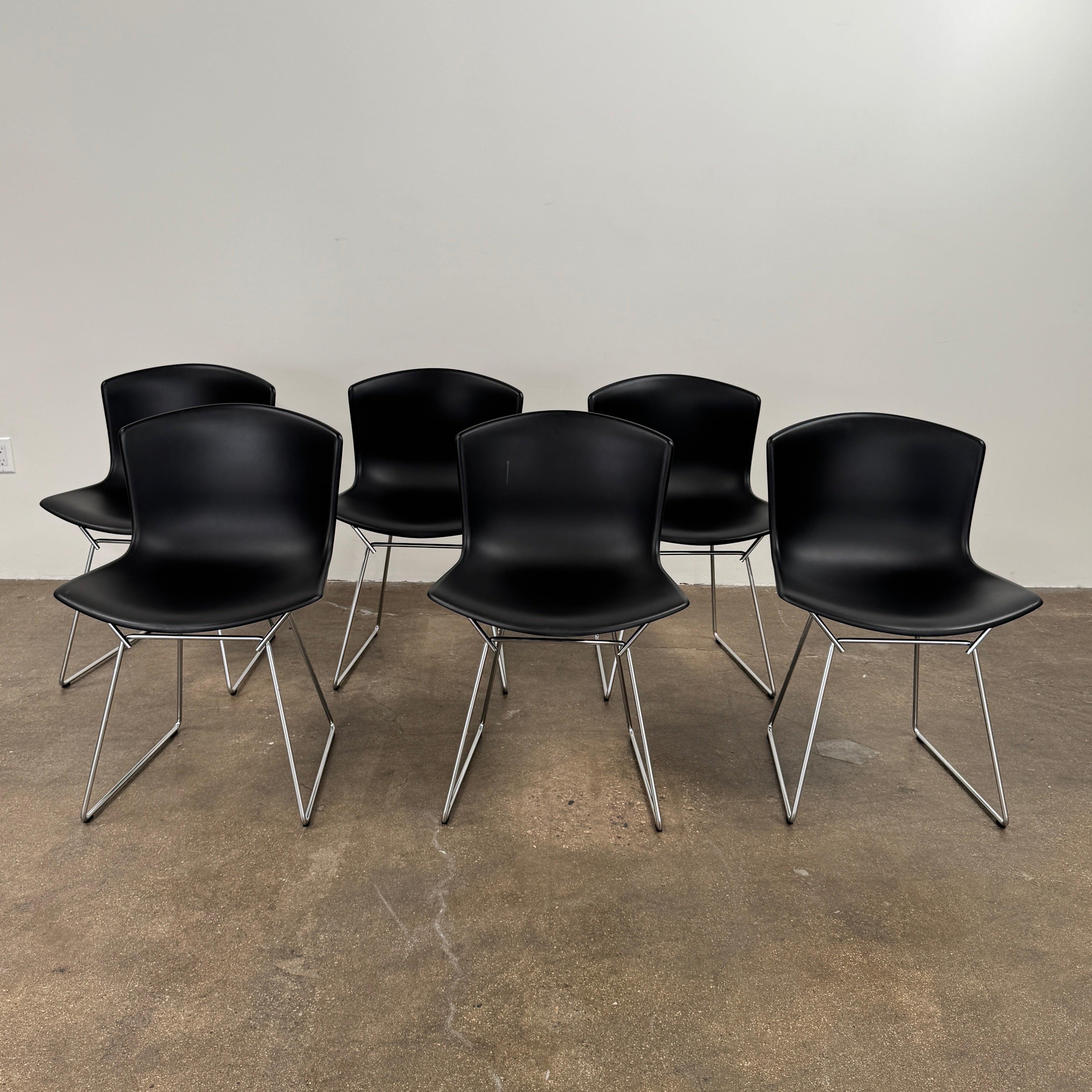 Eight Knoll Bertoia Molded Shell Chairs by Knoll, featuring black plastic seats and metal legs, are arranged in two rows on a white background, showcasing the sleek, timeless silhouette inspired by mid-century design.