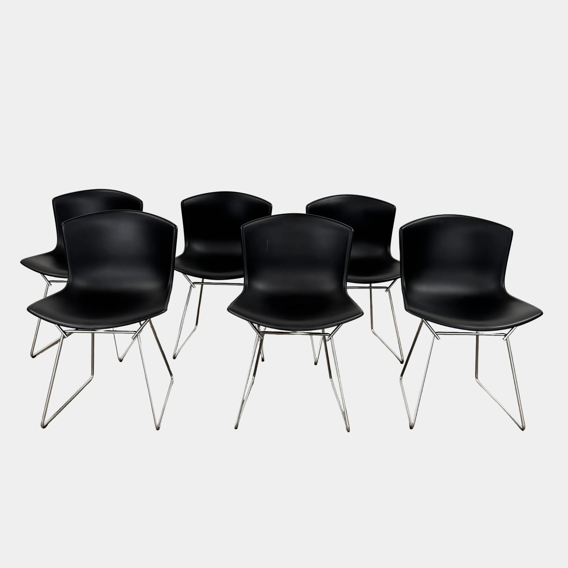 Eight Knoll Bertoia Molded Shell Chairs by Knoll, featuring black plastic seats and metal legs, are arranged in two rows on a white background, showcasing the sleek, timeless silhouette inspired by mid-century design.