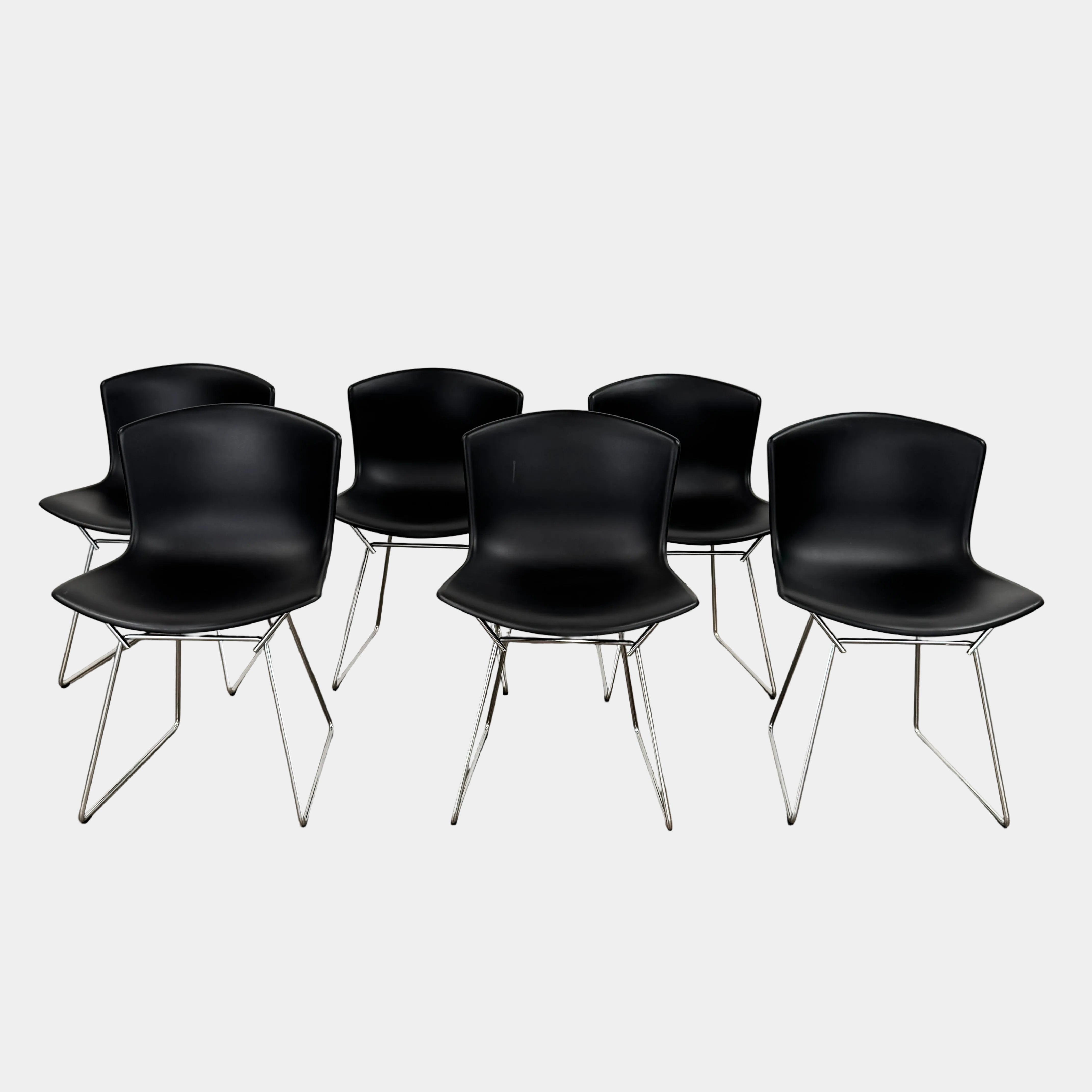 Eight Knoll Bertoia Molded Shell Chairs by Knoll, featuring black plastic seats and metal legs, are arranged in two rows on a white background, showcasing the sleek, timeless silhouette inspired by mid-century design.