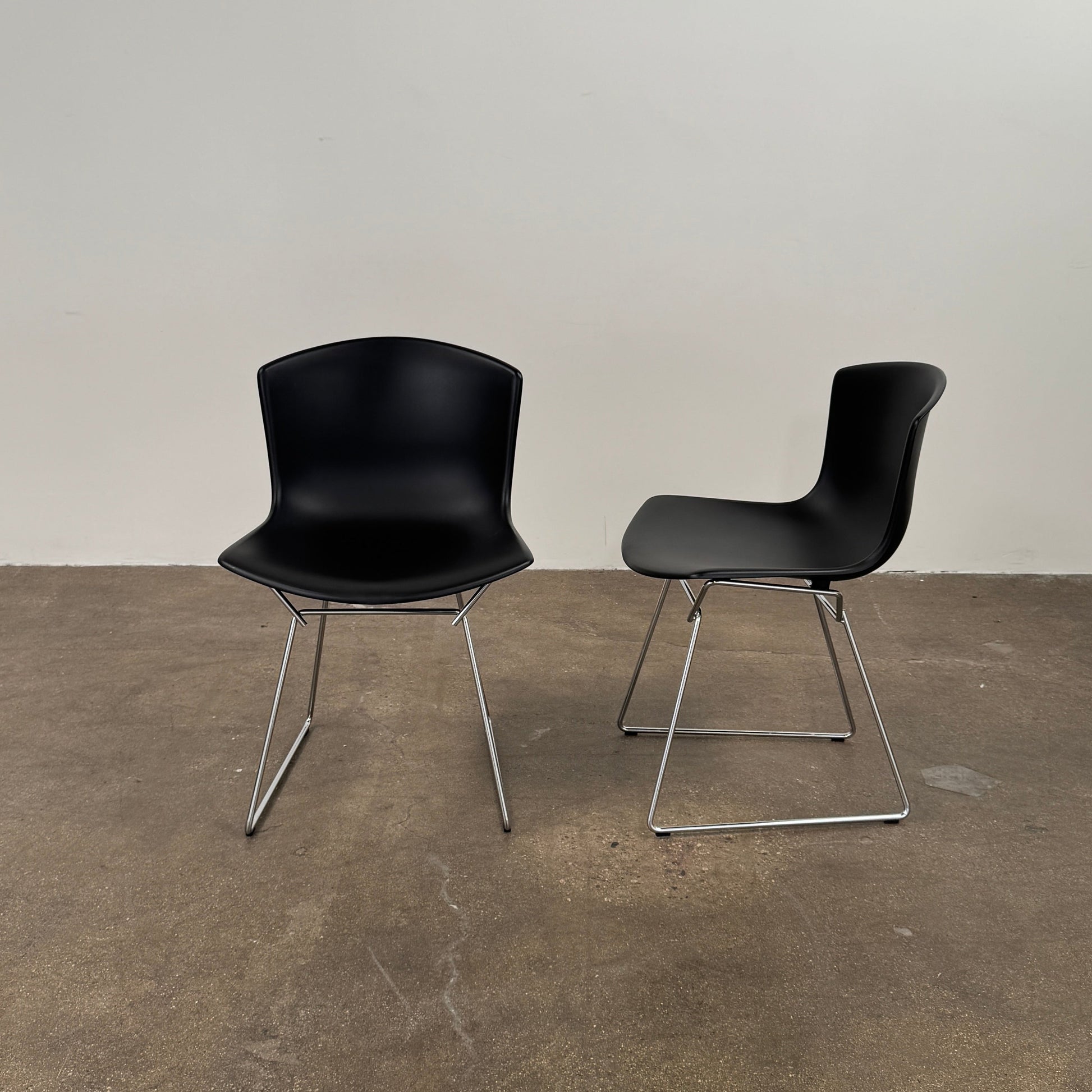 Eight Knoll Bertoia Molded Shell Chairs by Knoll, featuring black plastic seats and metal legs, are arranged in two rows on a white background, showcasing the sleek, timeless silhouette inspired by mid-century design.