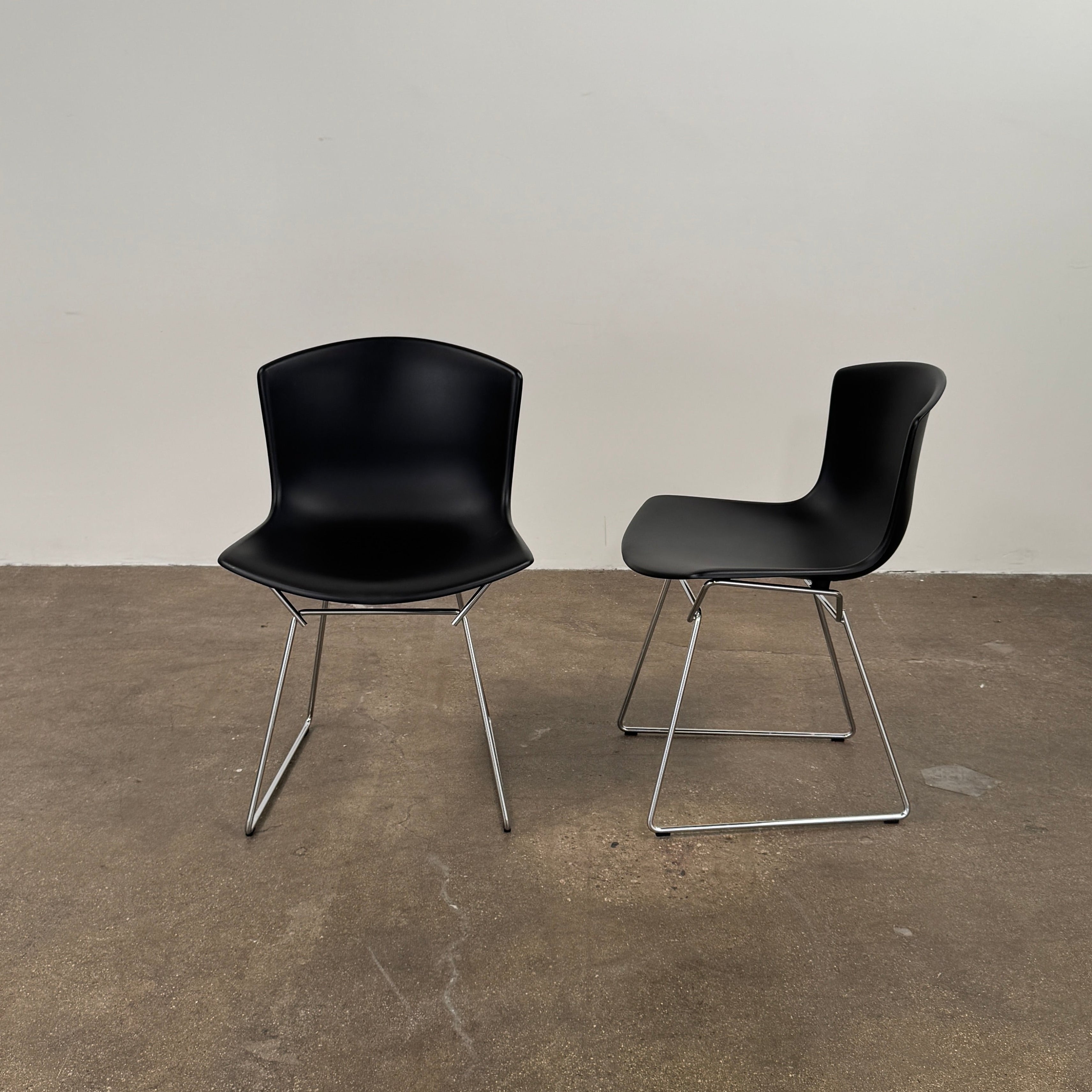 Eight Knoll Bertoia Molded Shell Chairs by Knoll, featuring black plastic seats and metal legs, are arranged in two rows on a white background, showcasing the sleek, timeless silhouette inspired by mid-century design.