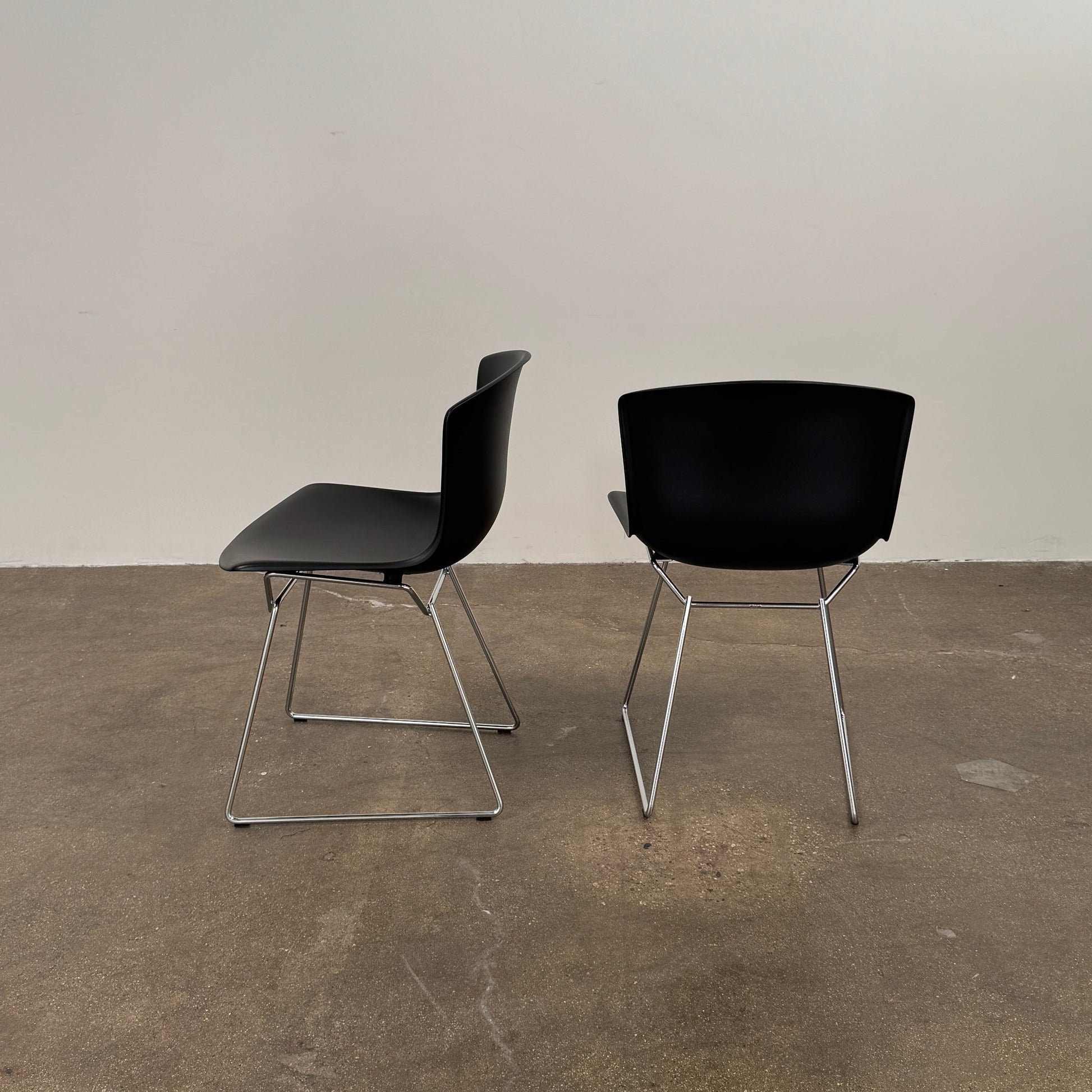 Eight Knoll Bertoia Molded Shell Chairs by Knoll, featuring black plastic seats and metal legs, are arranged in two rows on a white background, showcasing the sleek, timeless silhouette inspired by mid-century design.