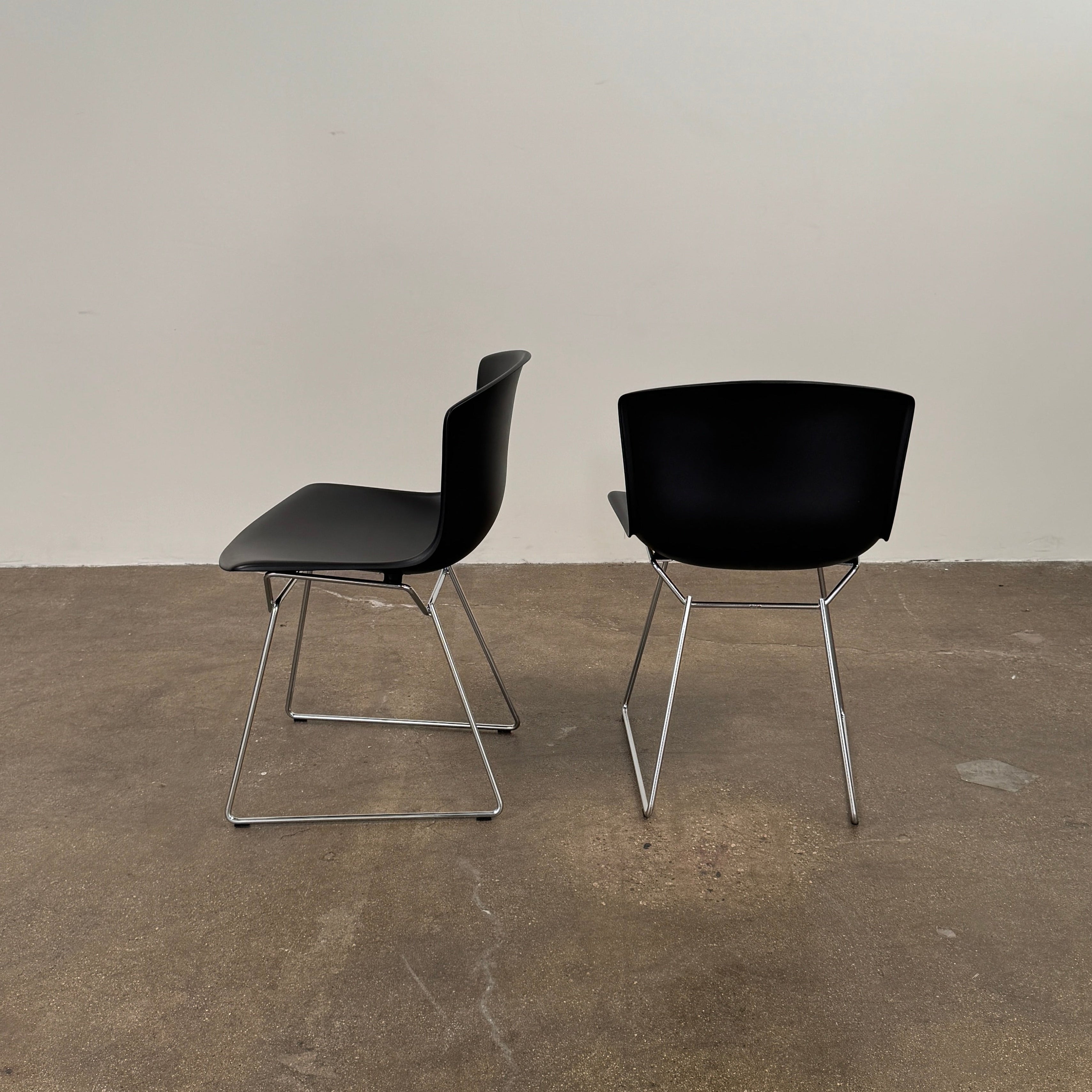 Eight Knoll Bertoia Molded Shell Chairs by Knoll, featuring black plastic seats and metal legs, are arranged in two rows on a white background, showcasing the sleek, timeless silhouette inspired by mid-century design.