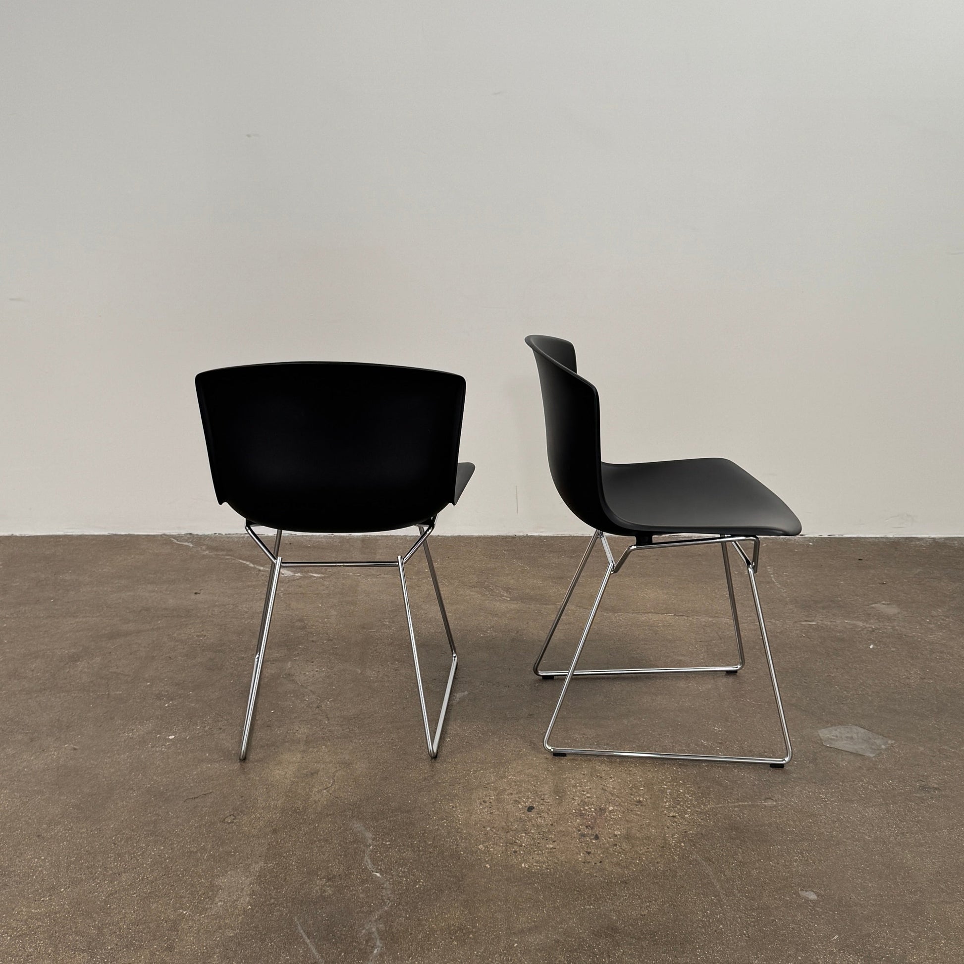 Eight Knoll Bertoia Molded Shell Chairs by Knoll, featuring black plastic seats and metal legs, are arranged in two rows on a white background, showcasing the sleek, timeless silhouette inspired by mid-century design.