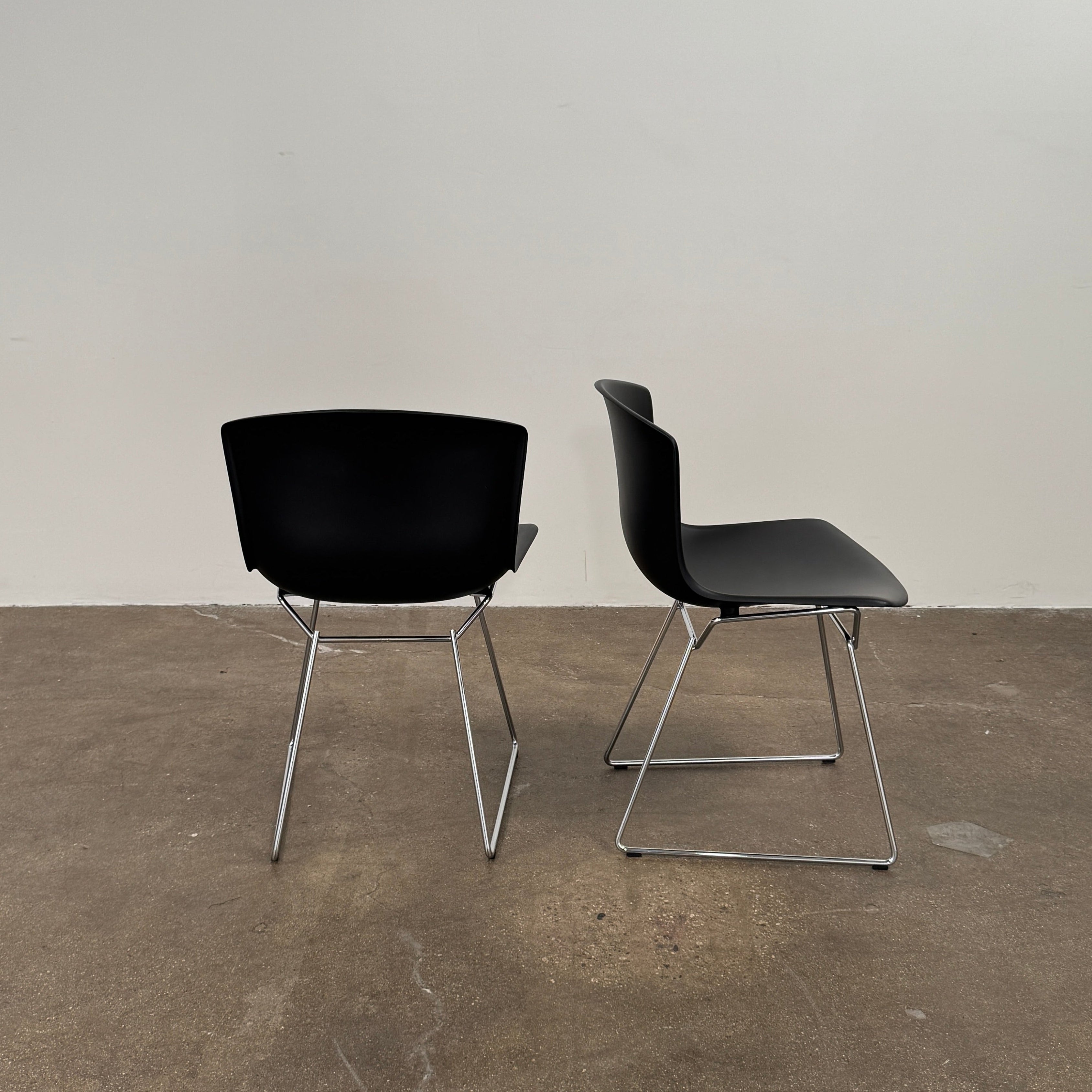 Eight Knoll Bertoia Molded Shell Chairs by Knoll, featuring black plastic seats and metal legs, are arranged in two rows on a white background, showcasing the sleek, timeless silhouette inspired by mid-century design.