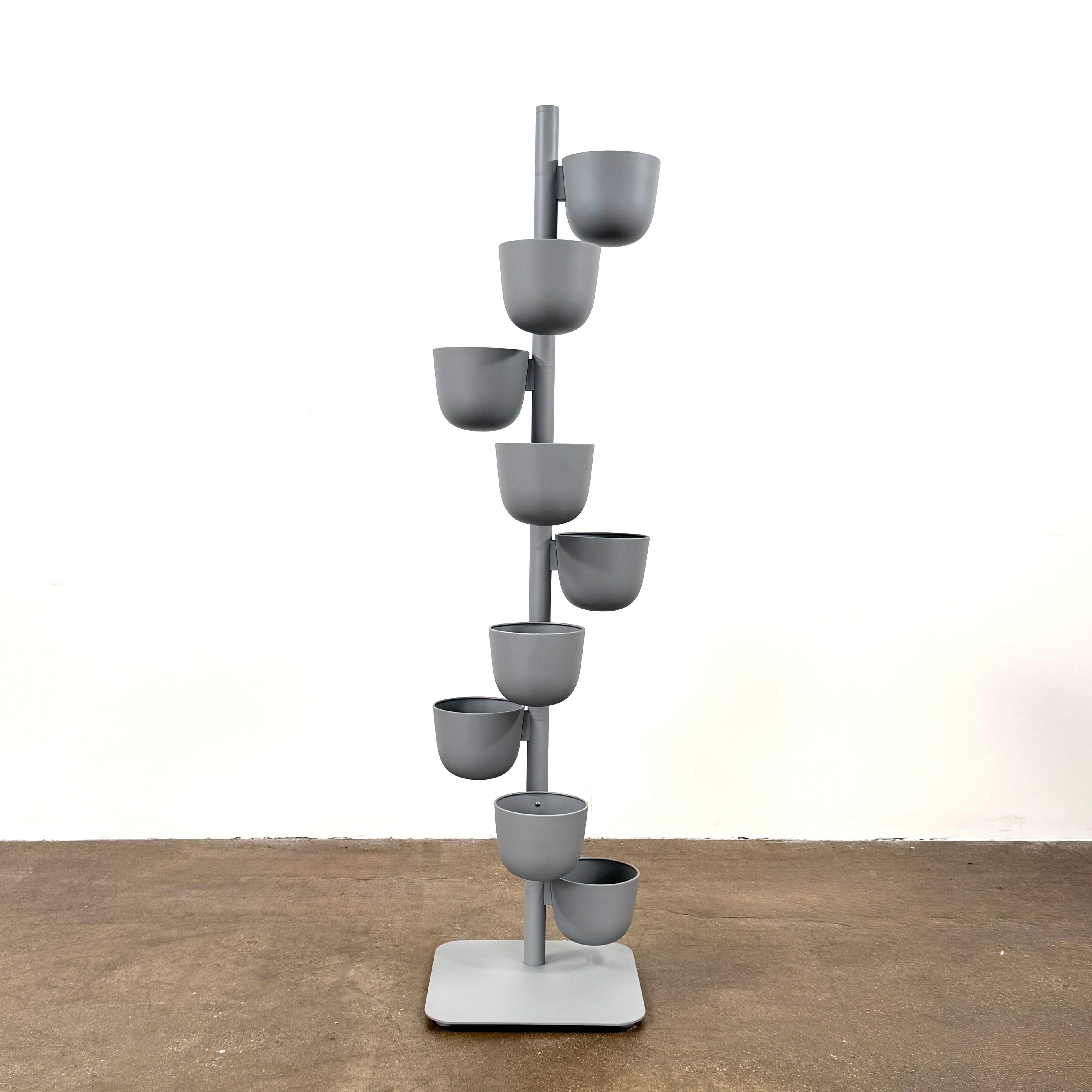 The DWR Story Planter by DWR is a vertical metal plant stand featuring eight gray round pots arranged in a staggered pattern along a single pole with a square base, making it an ideal decorative planter for fans of vertical gardening.