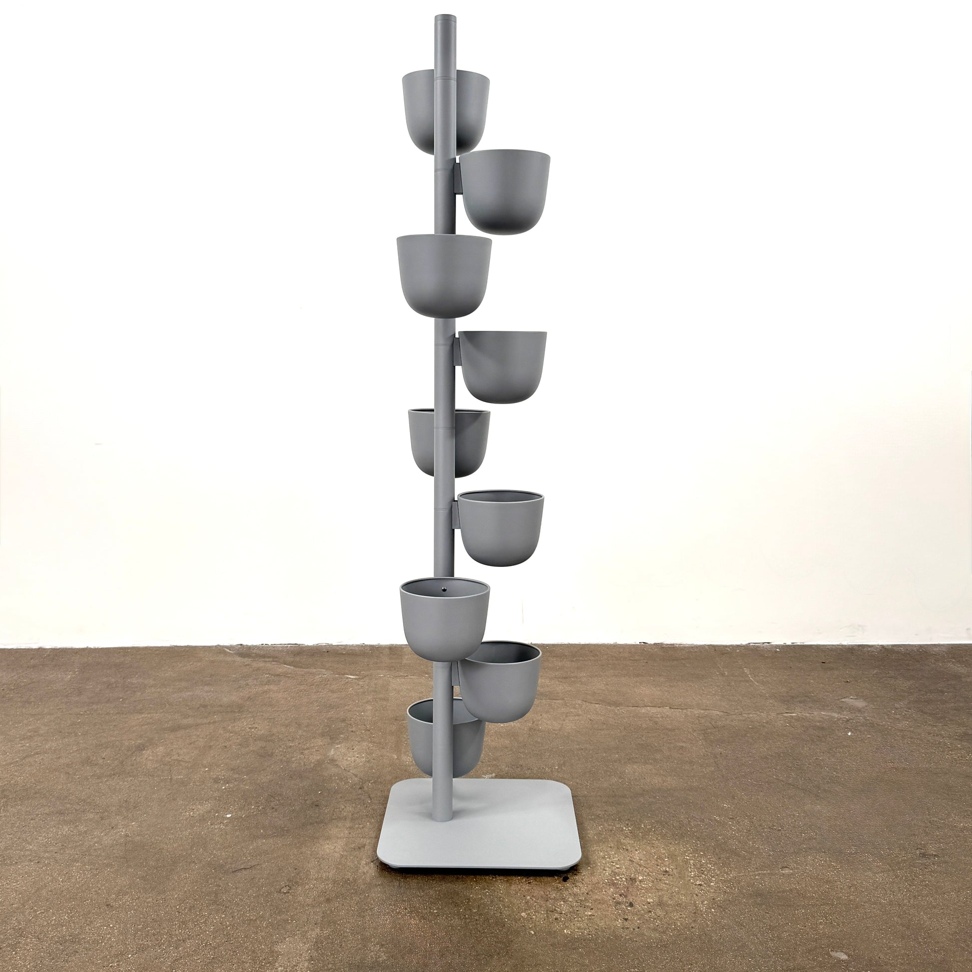 The DWR Story Planter by DWR is a vertical metal plant stand featuring eight gray round pots arranged in a staggered pattern along a single pole with a square base, making it an ideal decorative planter for fans of vertical gardening.