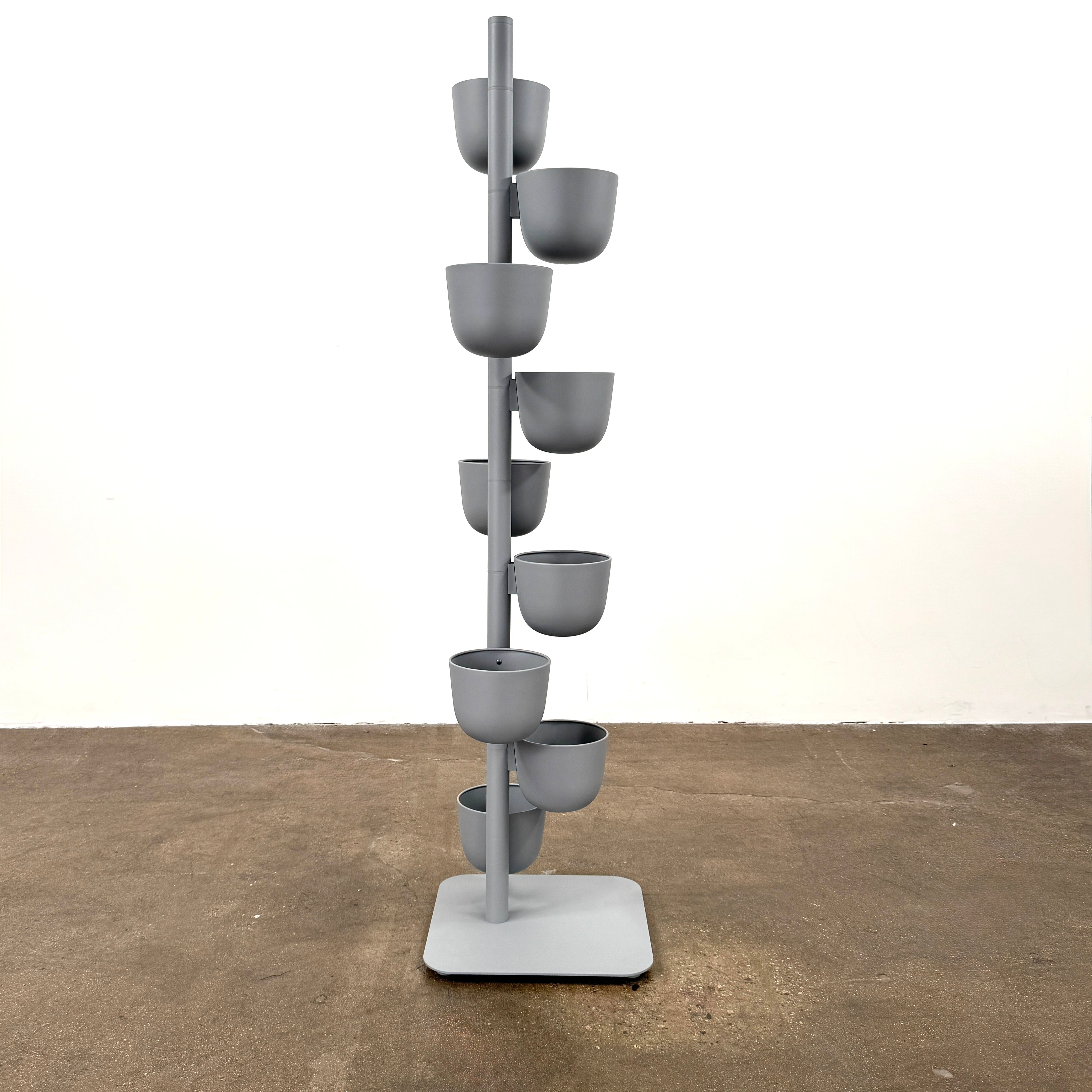 The DWR Story Planter by DWR is a vertical metal plant stand featuring eight gray round pots arranged in a staggered pattern along a single pole with a square base, making it an ideal decorative planter for fans of vertical gardening.