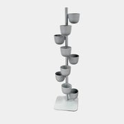 The DWR Story Planter by DWR is a vertical metal plant stand featuring eight gray round pots arranged in a staggered pattern along a single pole with a square base, making it an ideal decorative planter for fans of vertical gardening.