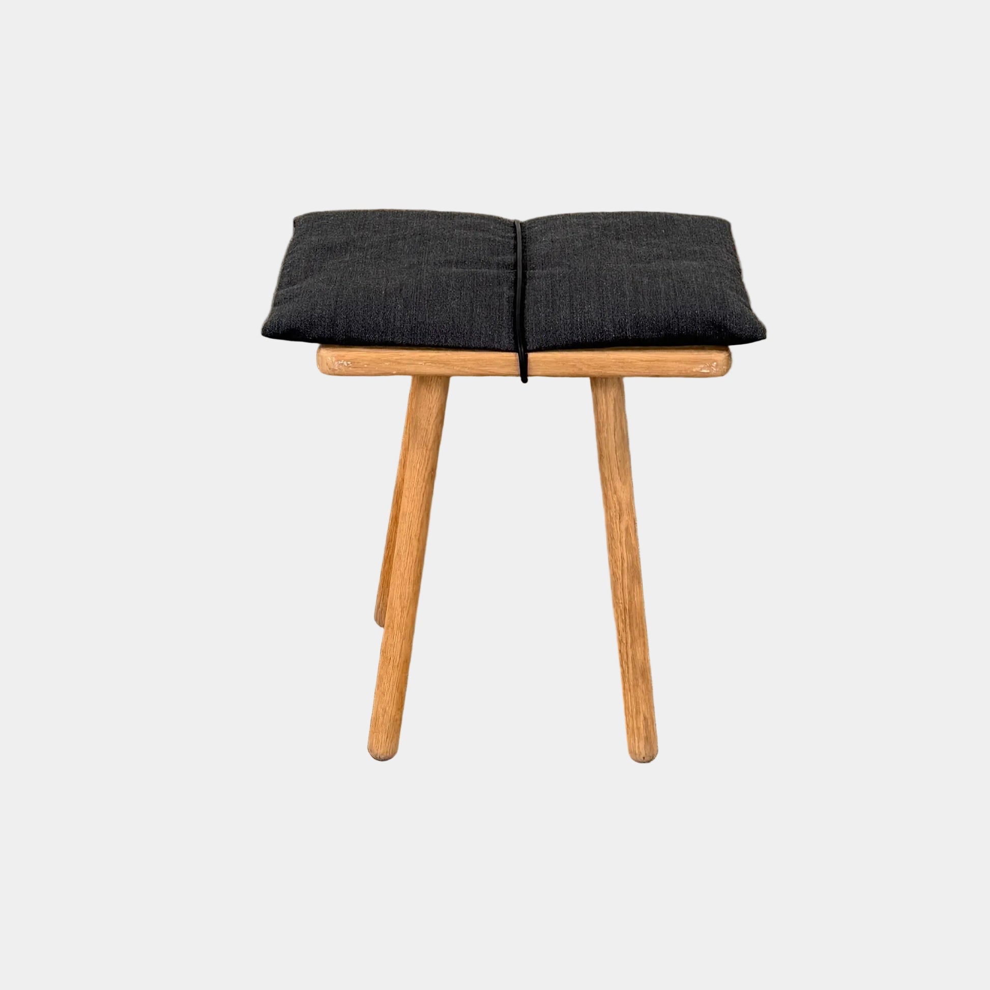 A Fritz Hansen Skagerak Georg Stool, featuring three wooden legs and a padded black cushion on top, is photographed against a plain white background.