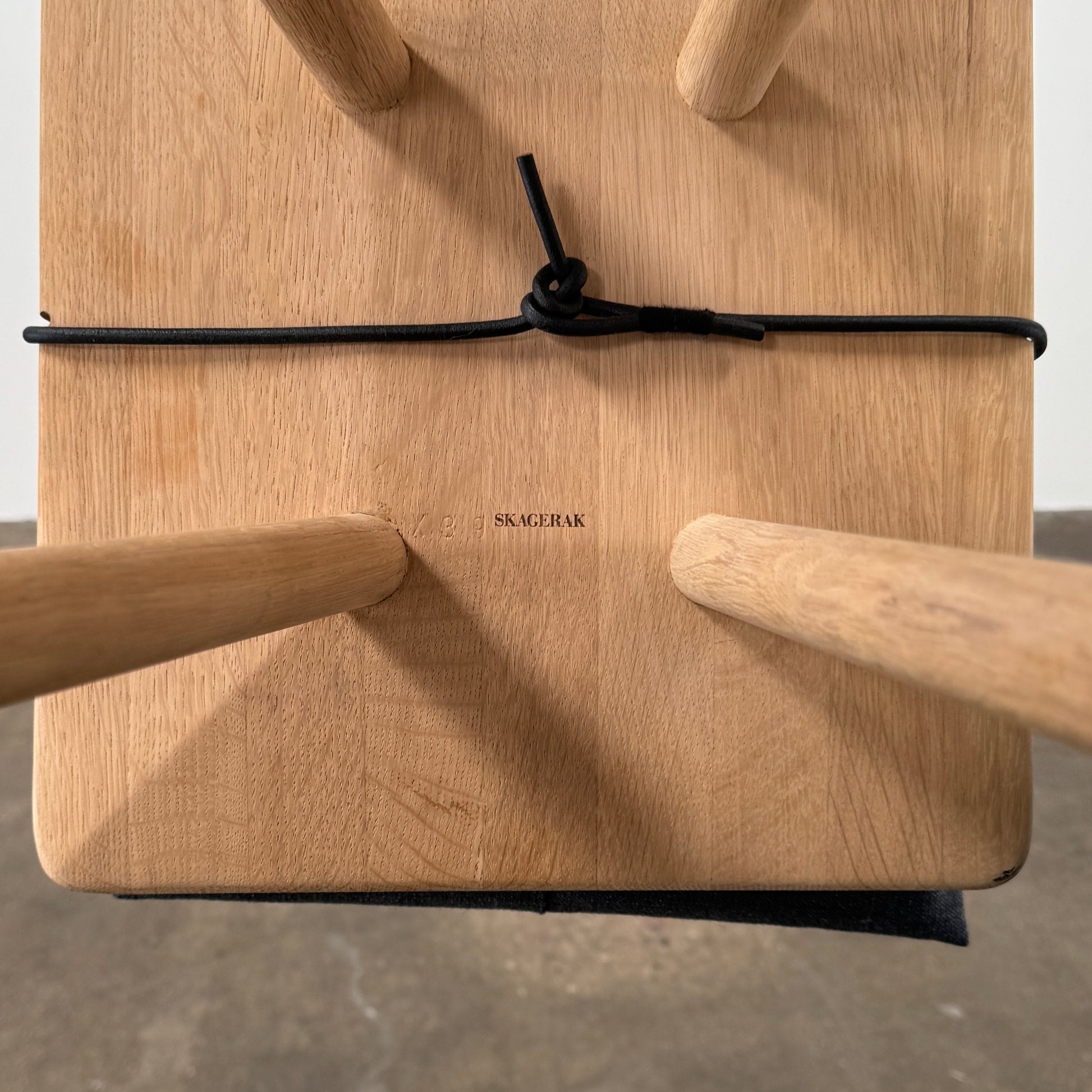 A Fritz Hansen Skagerak Georg Stool, featuring three wooden legs and a padded black cushion on top, is photographed against a plain white background.