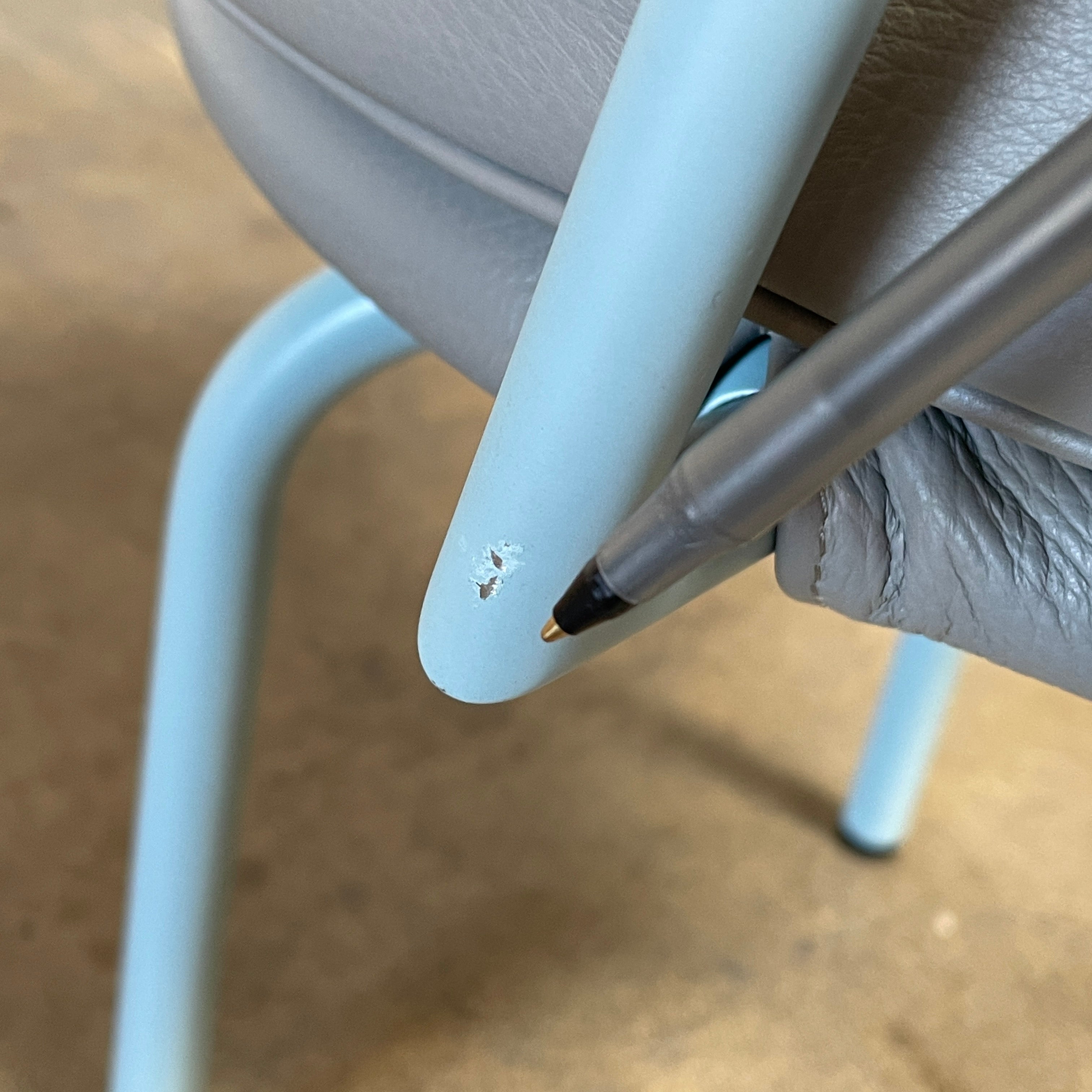 A gray leather Cassina LC7 Swivel Chair, featuring a circular seat, tubular backrest, and light blue metal legs, embodies modern design by Le Corbusier on a white background.