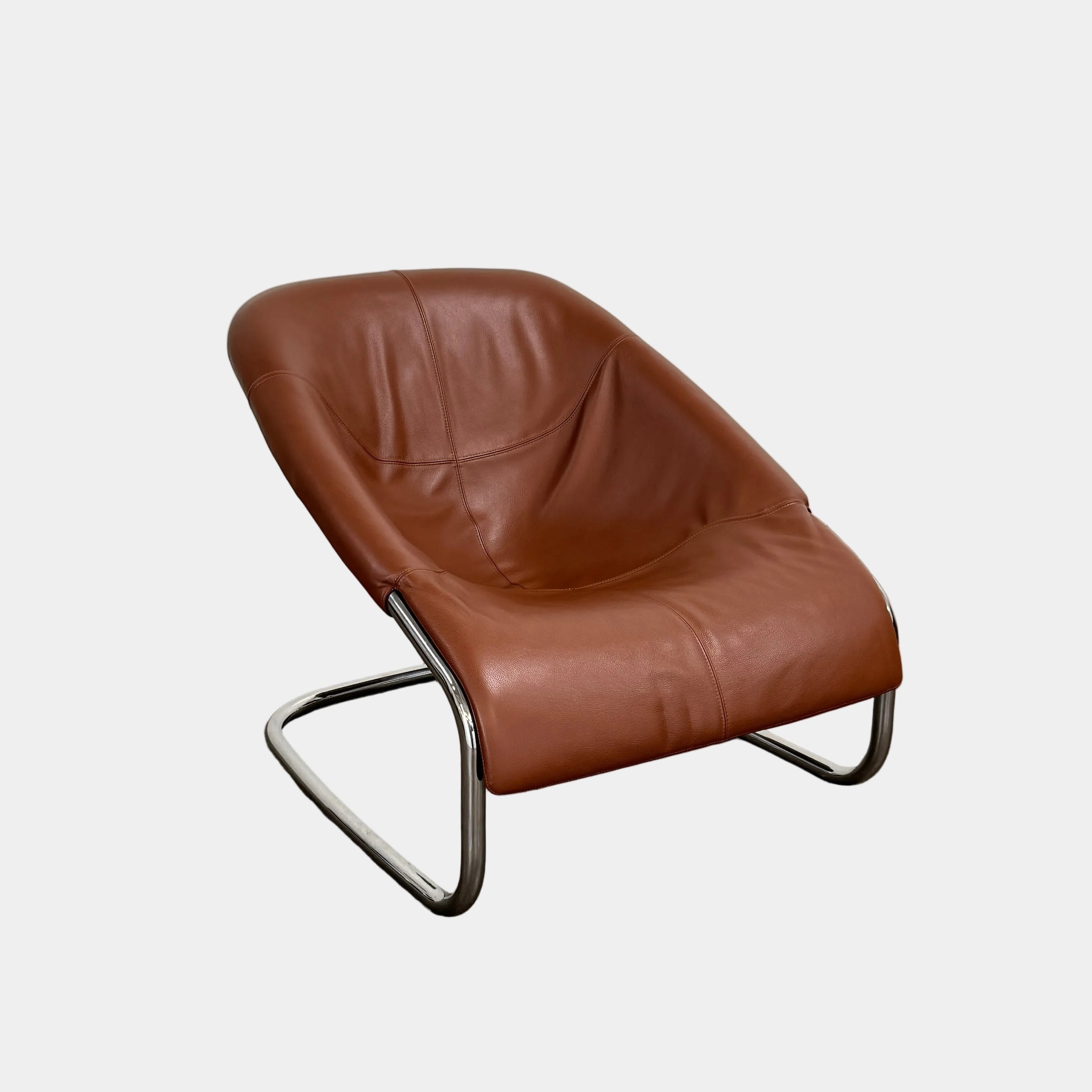 The Minotti Cortina Armchair by Minotti features luxurious brown leather upholstery and a gracefully curved seat, supported by a sleek chrome metal frame, and is showcased against a plain white background.