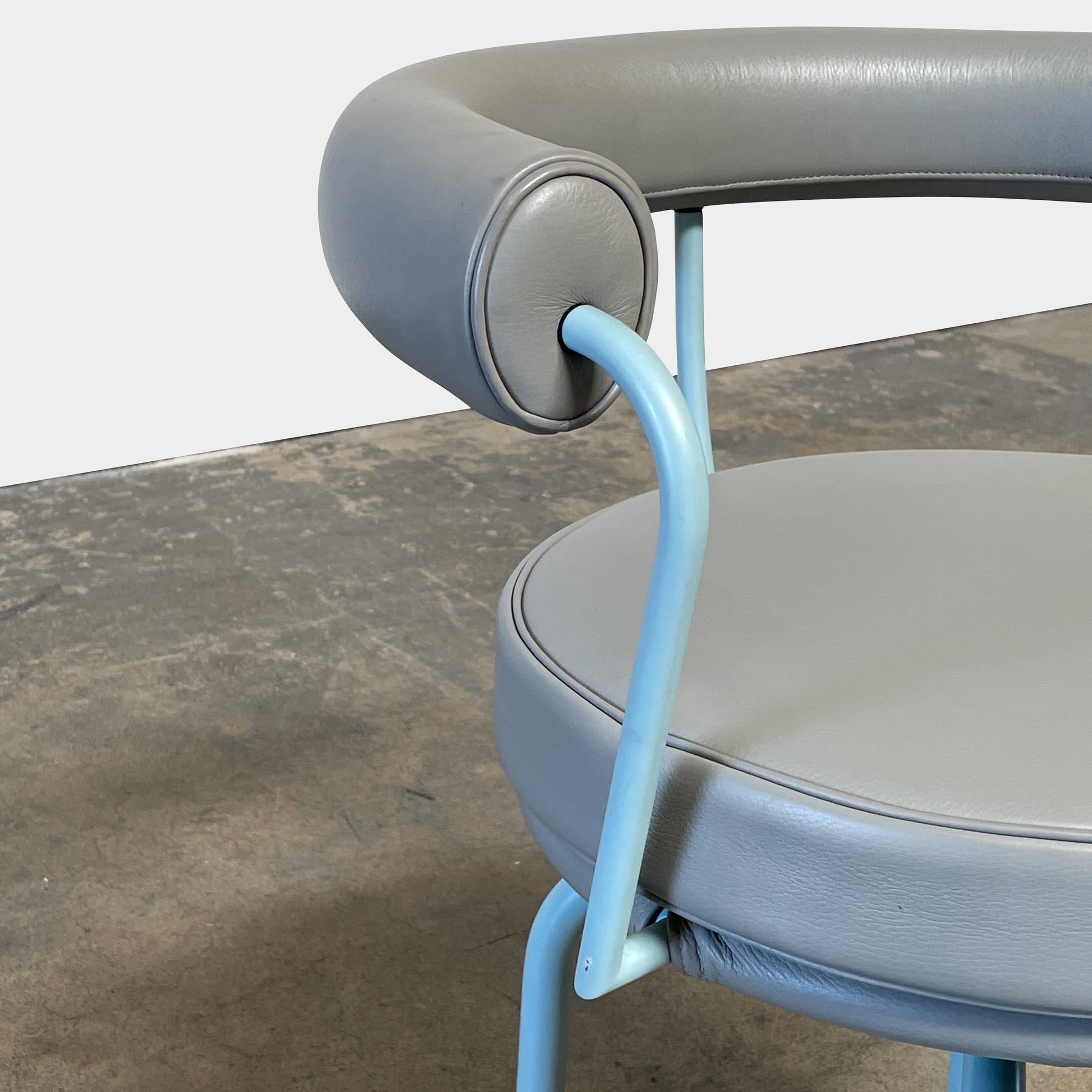A gray leather Cassina LC7 Swivel Chair, featuring a circular seat, tubular backrest, and light blue metal legs, embodies modern design by Le Corbusier on a white background.