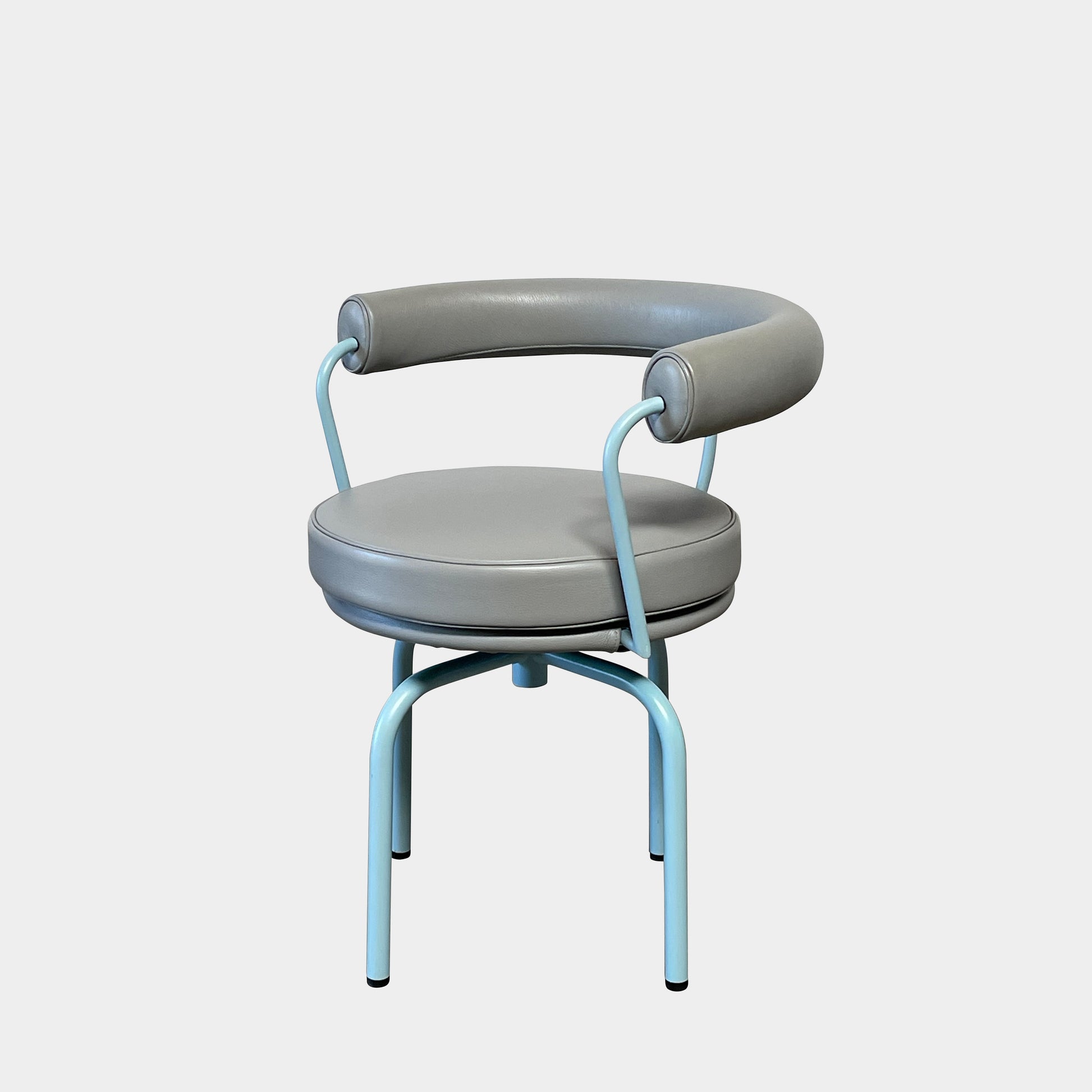 A gray leather Cassina LC7 Swivel Chair, featuring a circular seat, tubular backrest, and light blue metal legs, embodies modern design by Le Corbusier on a white background.
