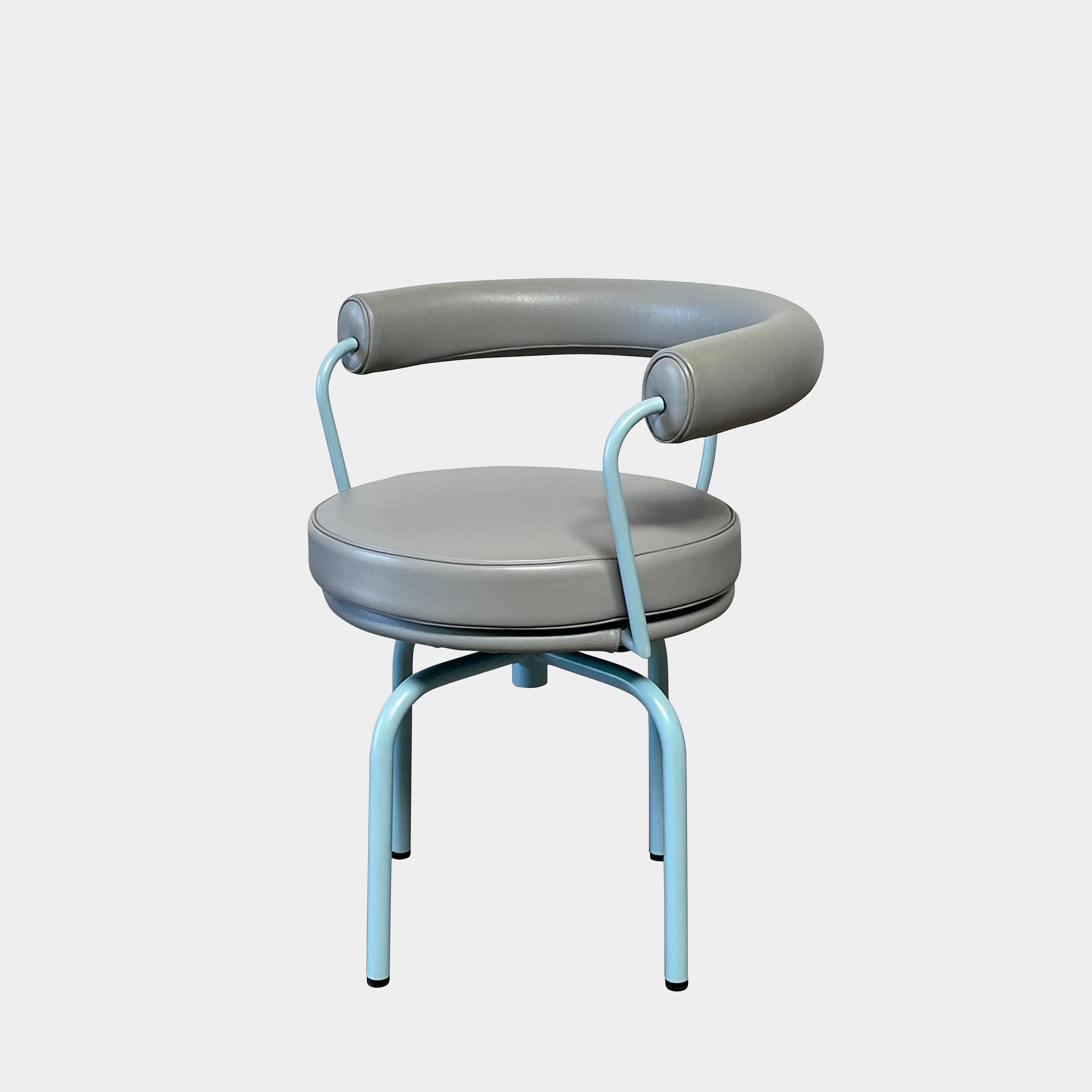 A gray leather Cassina LC7 Swivel Chair, featuring a circular seat, tubular backrest, and light blue metal legs, embodies modern design by Le Corbusier on a white background.