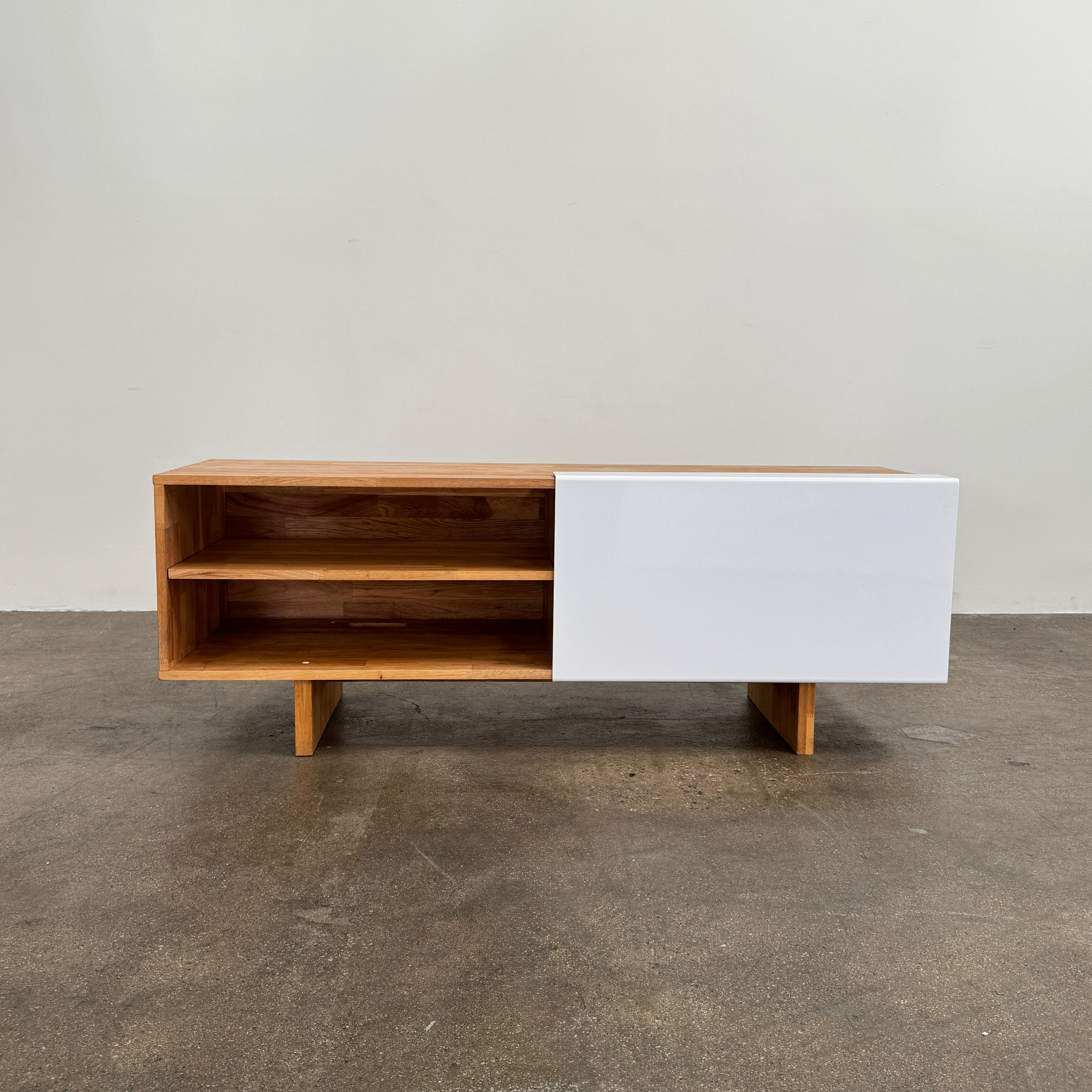 The Mash Studios LAXseries Media Console by Mash Studios is a modern wooden TV stand crafted from solid English walnut, featuring a sleek white sliding door, two open shelves with wire management for convenience, and distinctive angled legs, shown against a plain white background.