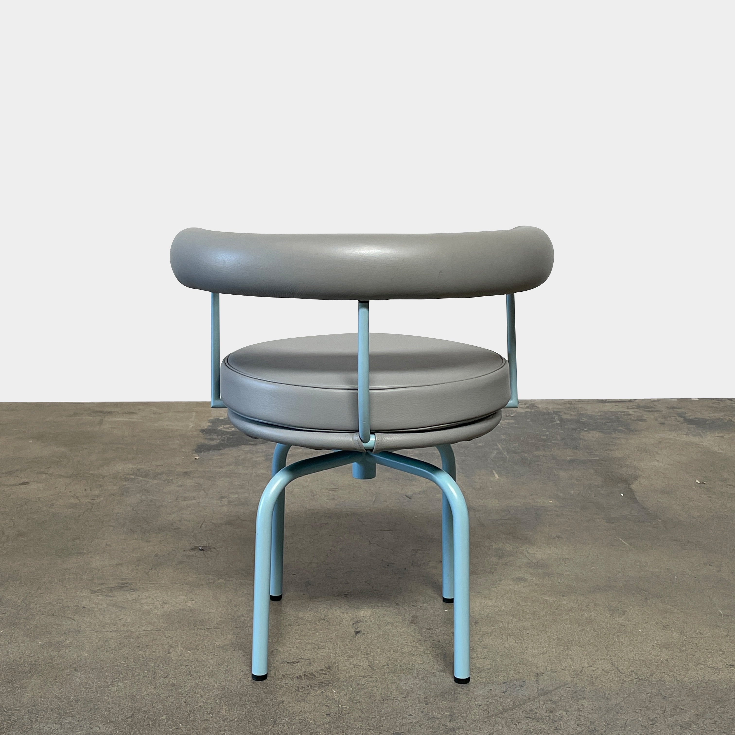 A gray leather Cassina LC7 Swivel Chair, featuring a circular seat, tubular backrest, and light blue metal legs, embodies modern design by Le Corbusier on a white background.