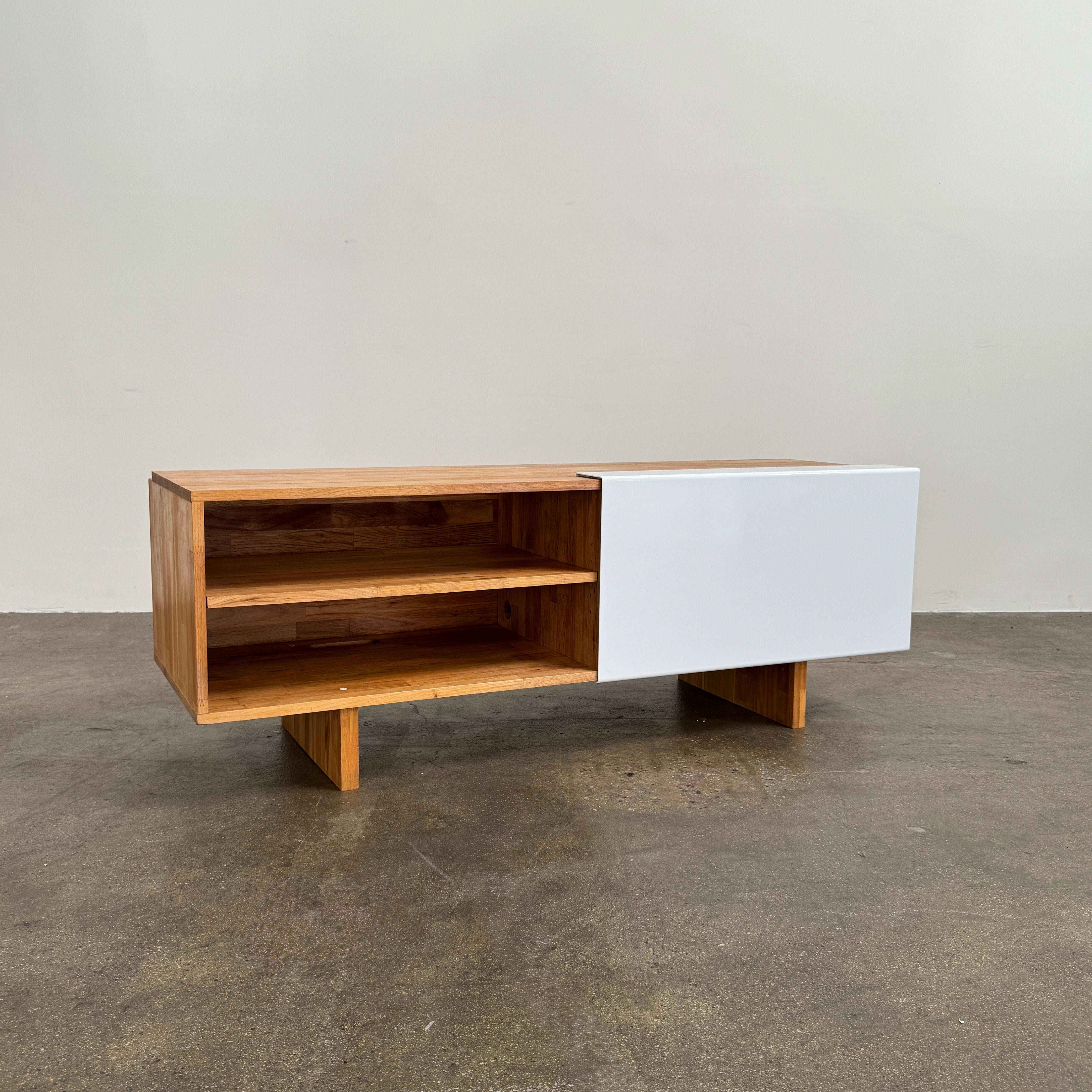 The Mash Studios LAXseries Media Console by Mash Studios is a modern wooden TV stand crafted from solid English walnut, featuring a sleek white sliding door, two open shelves with wire management for convenience, and distinctive angled legs, shown against a plain white background.