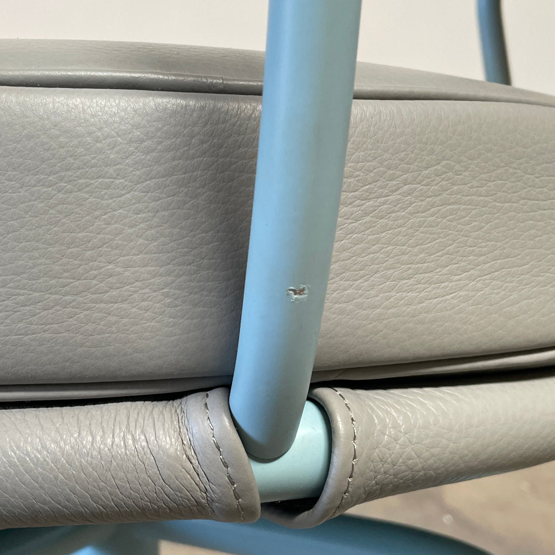 A gray leather Cassina LC7 Swivel Chair, featuring a circular seat, tubular backrest, and light blue metal legs, embodies modern design by Le Corbusier on a white background.