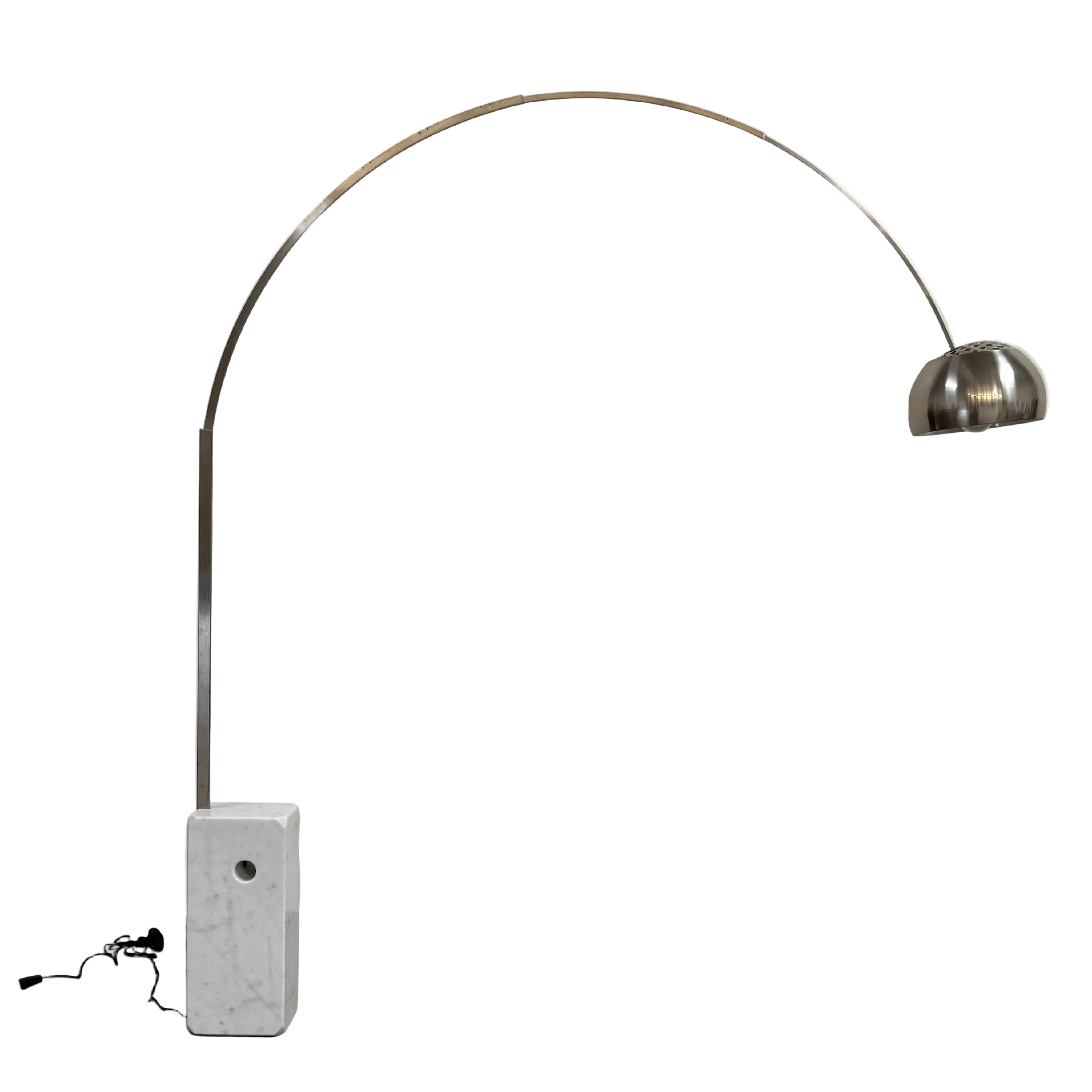 The DWR Arco Floor Lamp by DWR features a marble base, a sleek metal arching stem, and a dome-shaped metal shade; inspired by Italian craftsmanship and Achille Castiglioni’s legendary design, with an electrical cord and plug visible near the base.