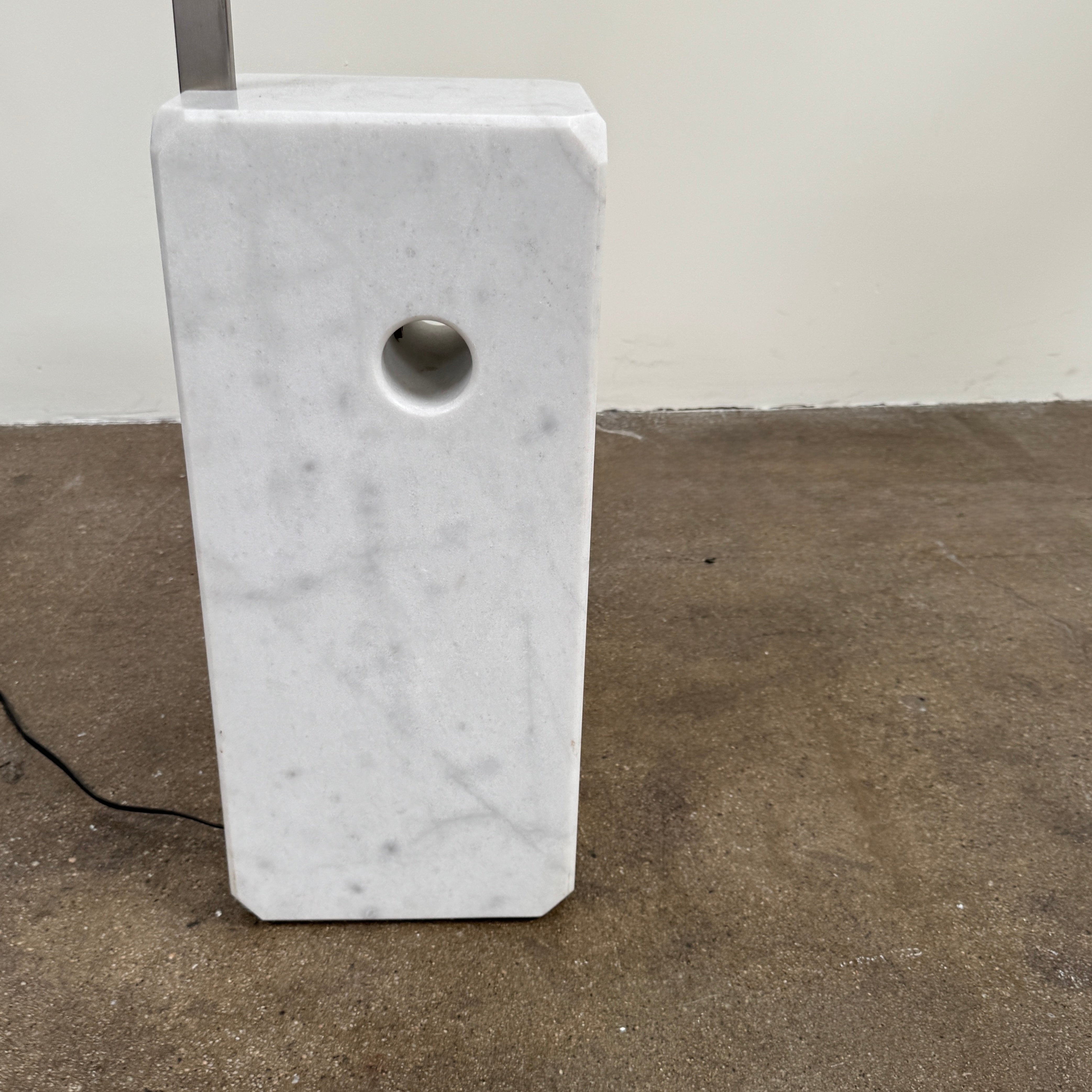 The DWR Arco Floor Lamp by DWR features a marble base, a sleek metal arching stem, and a dome-shaped metal shade; inspired by Italian craftsmanship and Achille Castiglioni’s legendary design, with an electrical cord and plug visible near the base.