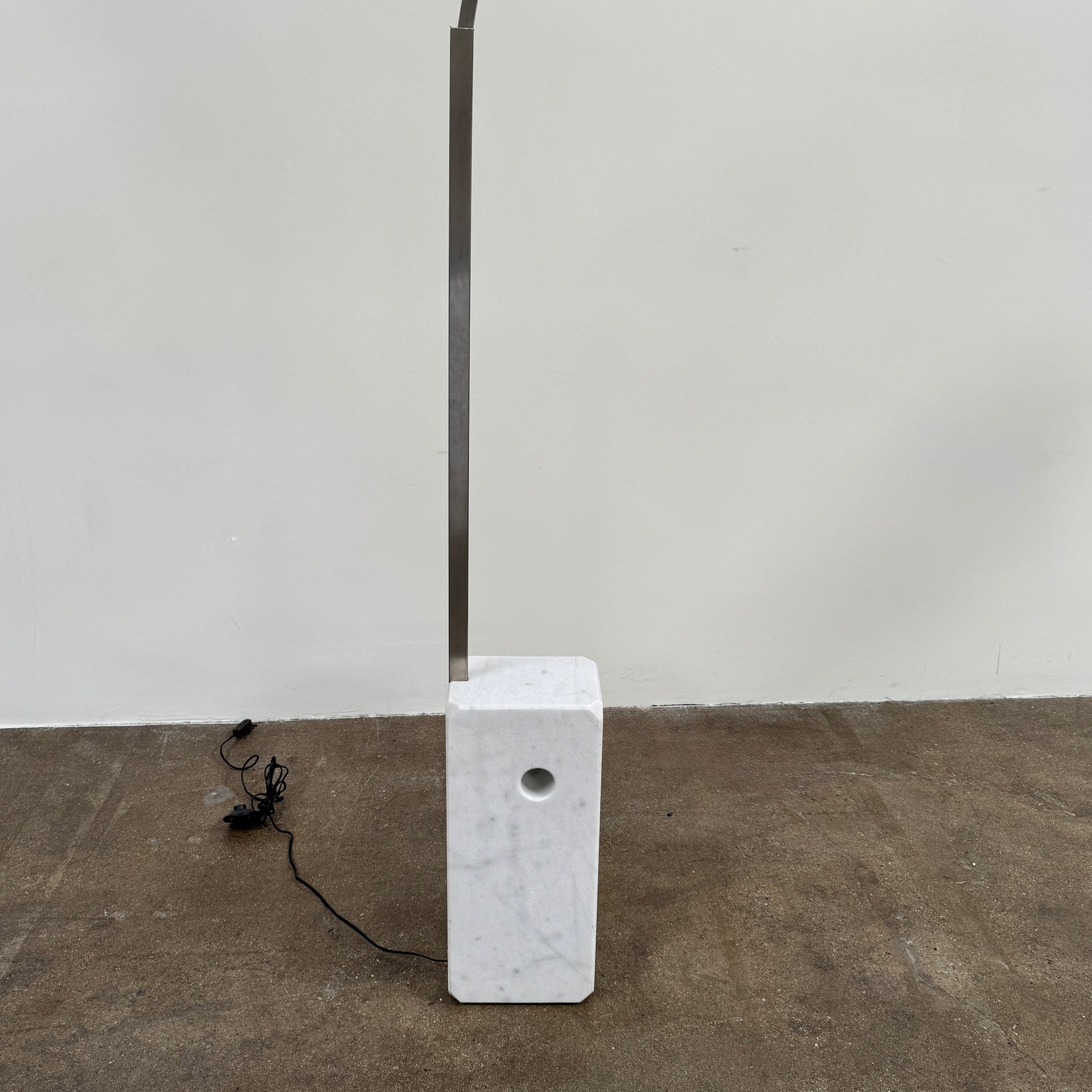 The DWR Arco Floor Lamp by DWR features a marble base, a sleek metal arching stem, and a dome-shaped metal shade; inspired by Italian craftsmanship and Achille Castiglioni’s legendary design, with an electrical cord and plug visible near the base.