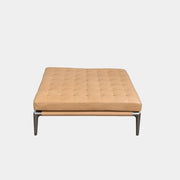 The Cassina Prive Ottoman by Cassina is a rectangular tan leather luxury ottoman featuring tufted upholstery and sleek metal legs, displayed against a plain white background.