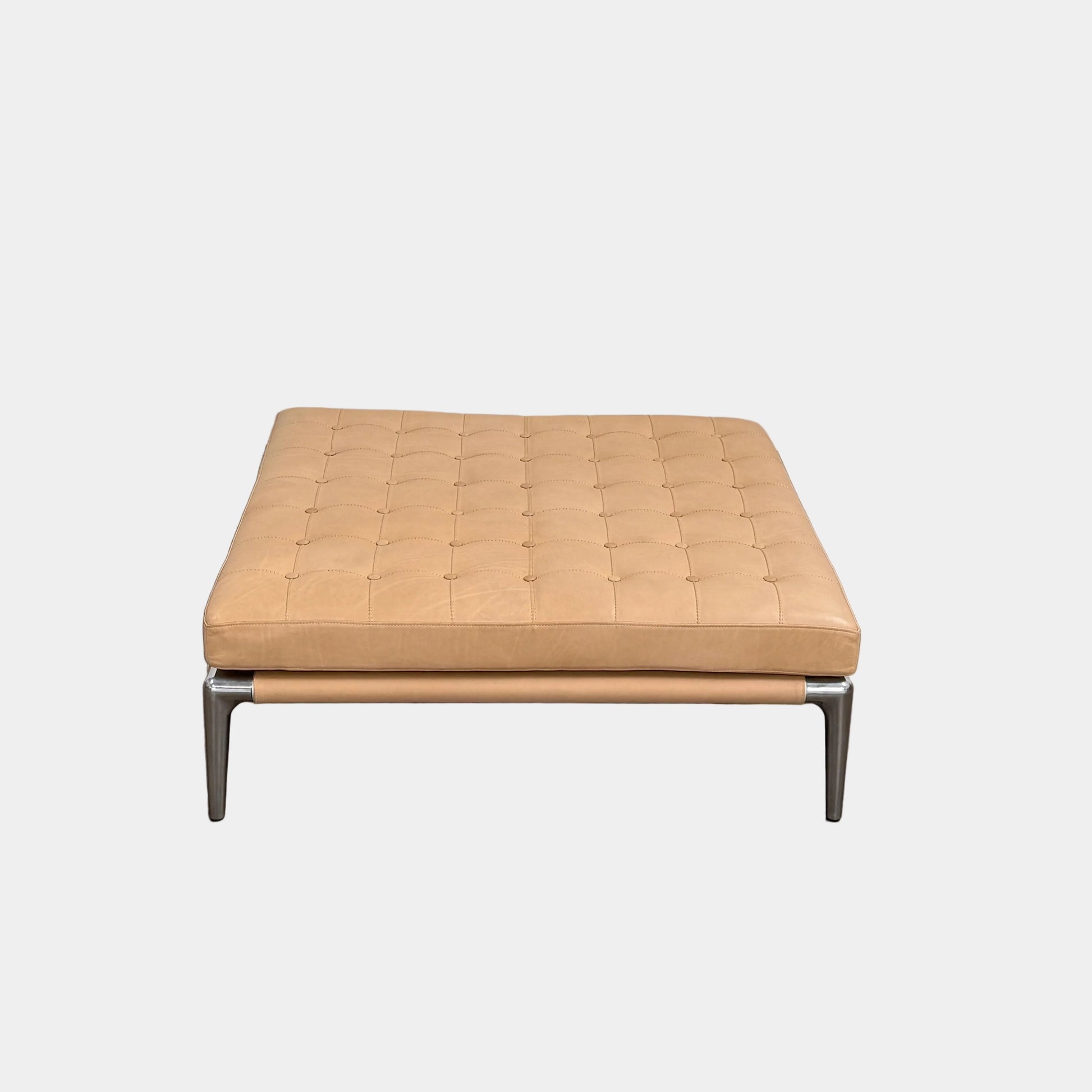 The Cassina Prive Ottoman by Cassina is a rectangular tan leather luxury ottoman featuring tufted upholstery and sleek metal legs, displayed against a plain white background.
