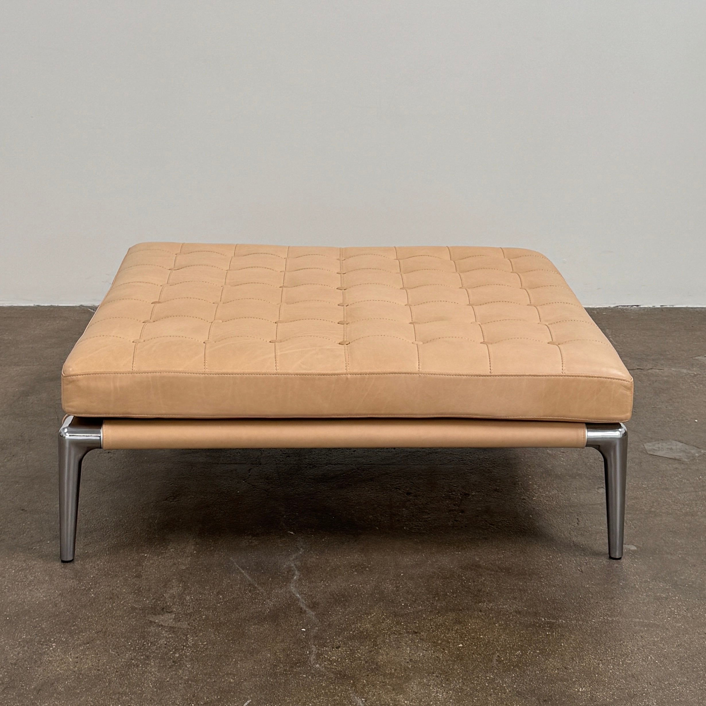 The Cassina Prive Ottoman by Cassina is a rectangular tan leather luxury ottoman featuring tufted upholstery and sleek metal legs, displayed against a plain white background.