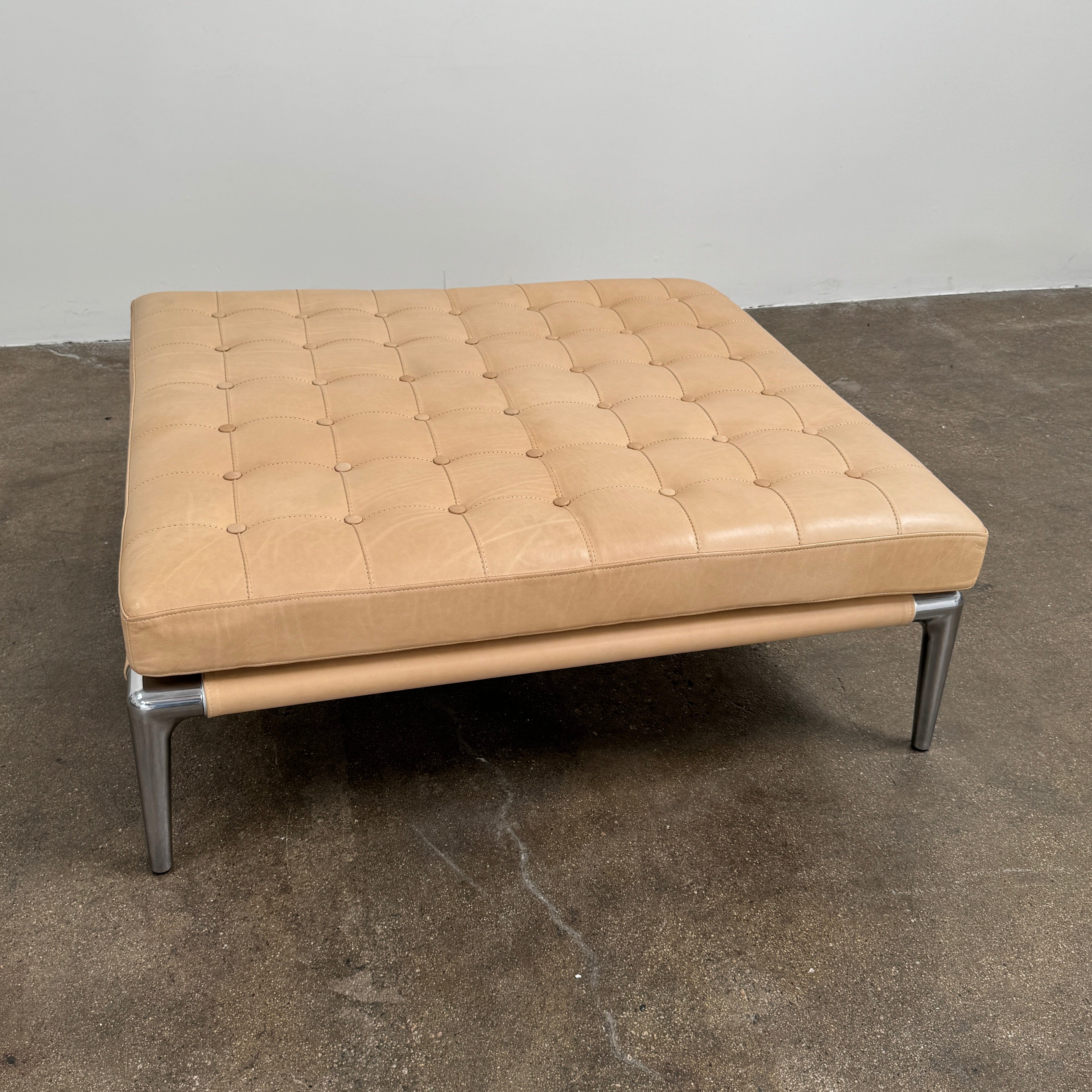 The Cassina Prive Ottoman by Cassina is a rectangular tan leather luxury ottoman featuring tufted upholstery and sleek metal legs, displayed against a plain white background.