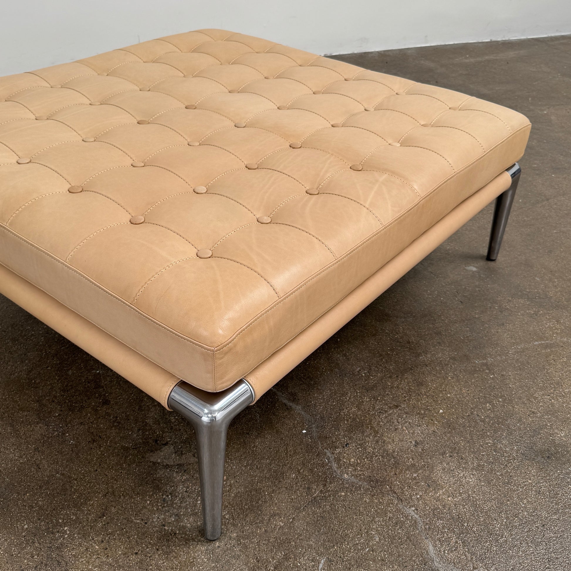 The Cassina Prive Ottoman by Cassina is a rectangular tan leather luxury ottoman featuring tufted upholstery and sleek metal legs, displayed against a plain white background.