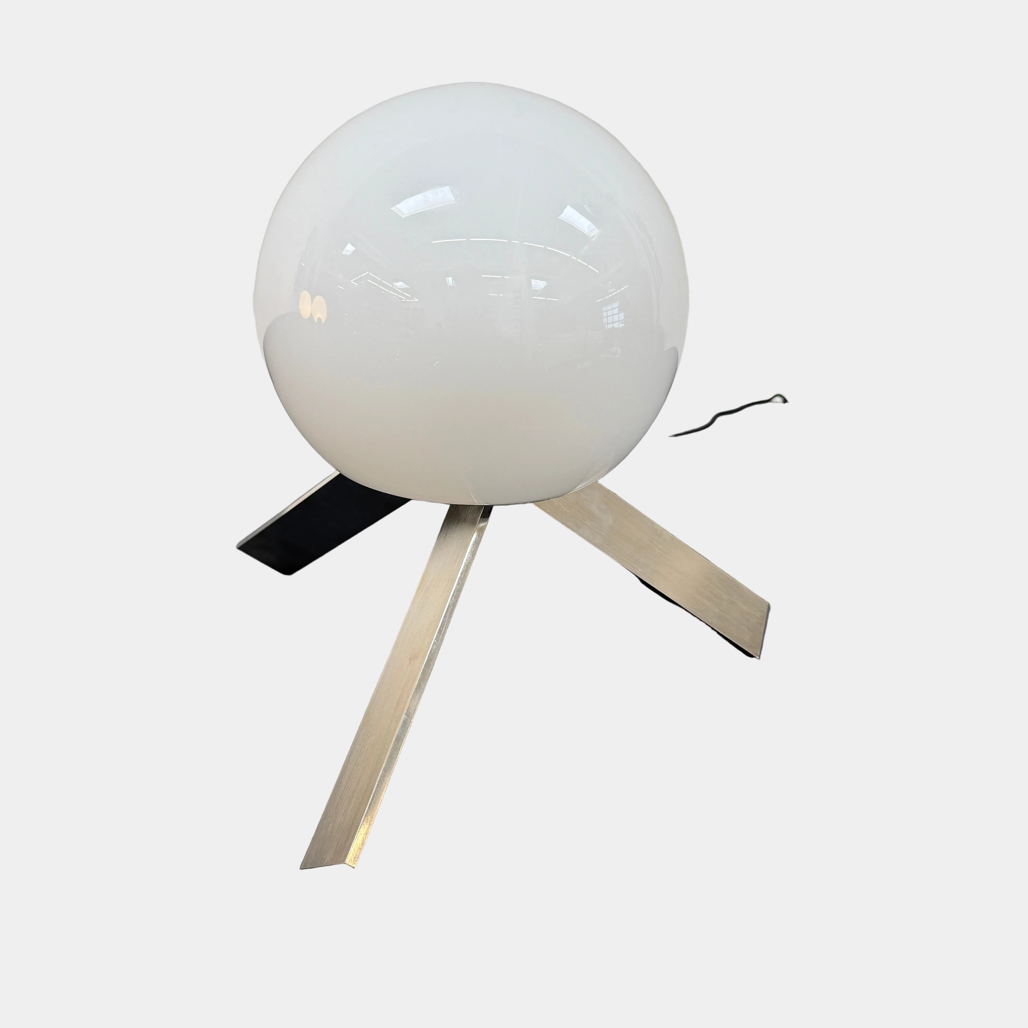 The Michael Anastassiades To The Top Table Lamp features a spherical white opaline glass shade and sits on three gold angled legs, designed by Michael Anastassiades, set against a plain light background.