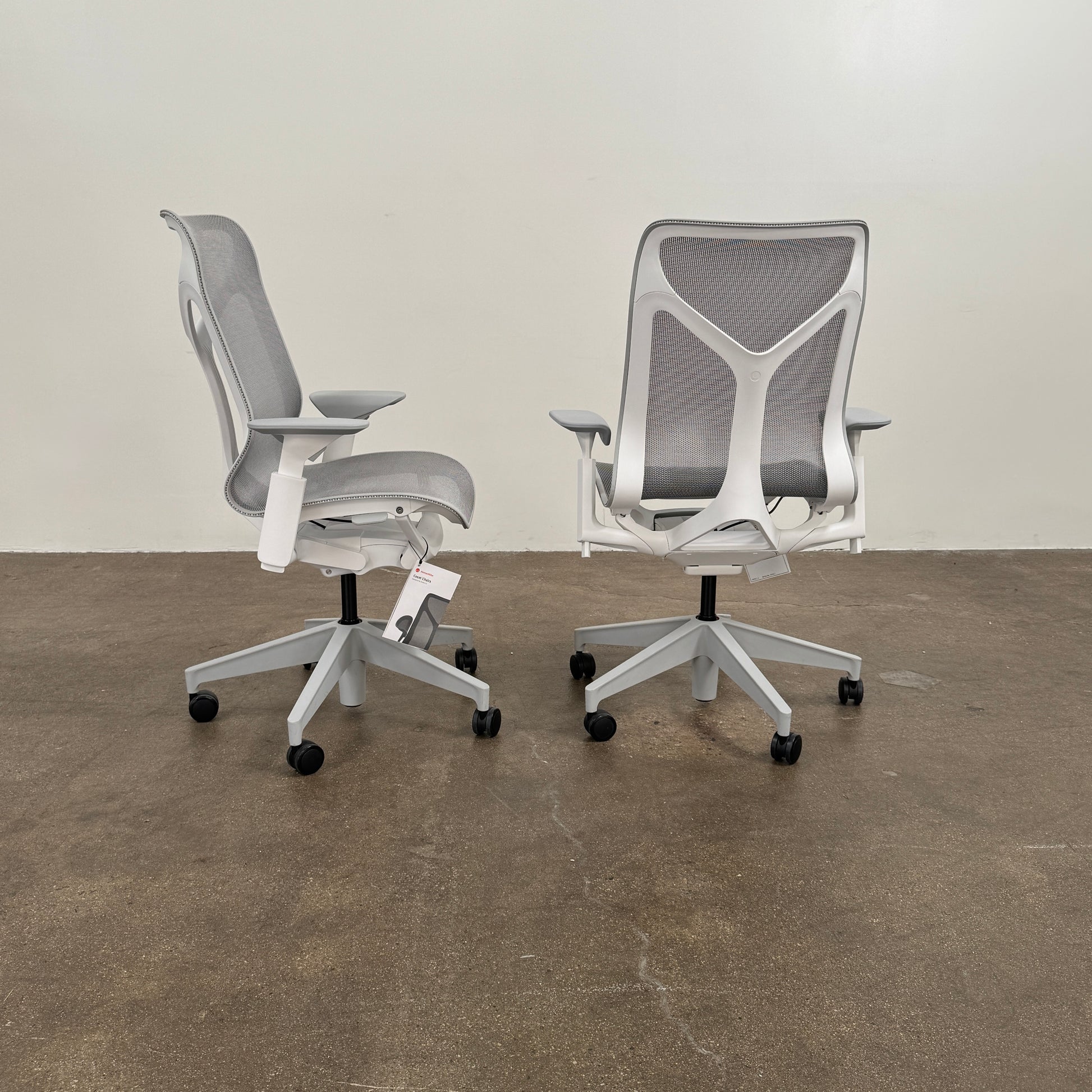 A sleek, modern white Herman Miller Cosm Office Chair featuring a mesh back and seat, supportive armrests, and five caster wheels is showcased on a concrete floor against an off-white wall. Designed by Herman Miller, this ergonomic chair seamlessly combines contemporary style with exceptional comfort.