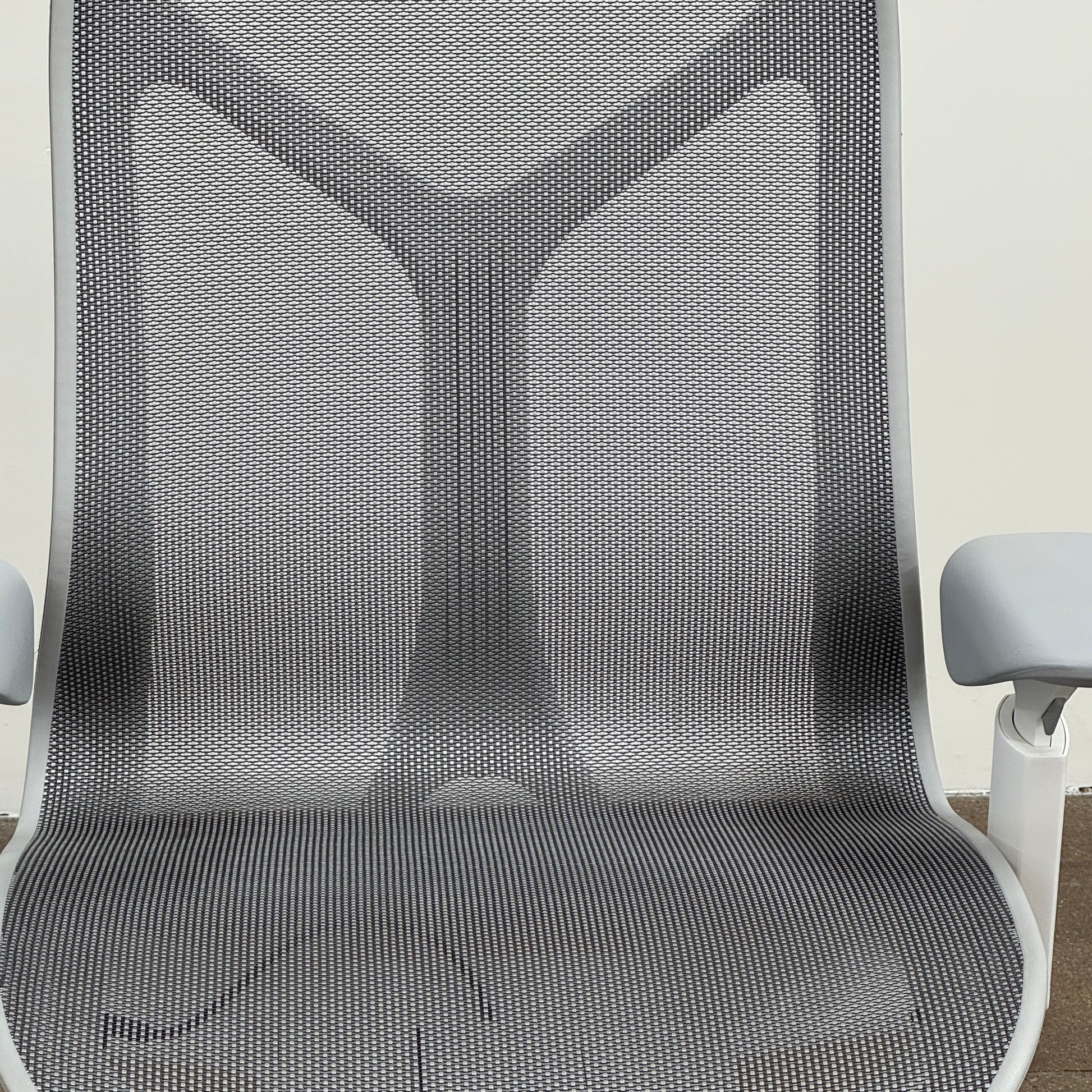 A sleek, modern white Herman Miller Cosm Office Chair featuring a mesh back and seat, supportive armrests, and five caster wheels is showcased on a concrete floor against an off-white wall. Designed by Herman Miller, this ergonomic chair seamlessly combines contemporary style with exceptional comfort.