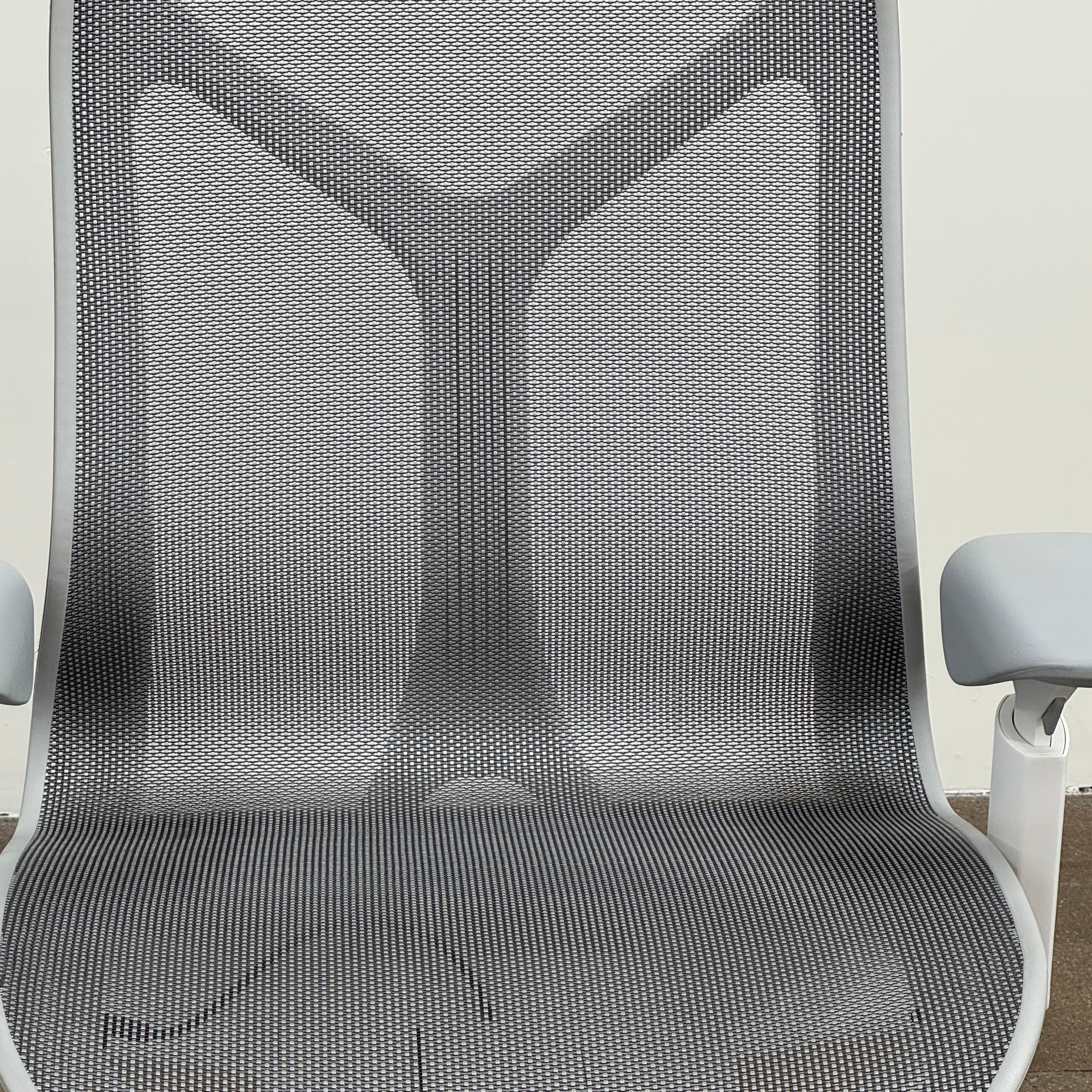 A sleek, modern white Herman Miller Cosm Office Chair featuring a mesh back and seat, supportive armrests, and five caster wheels is showcased on a concrete floor against an off-white wall. Designed by Herman Miller, this ergonomic chair seamlessly combines contemporary style with exceptional comfort.