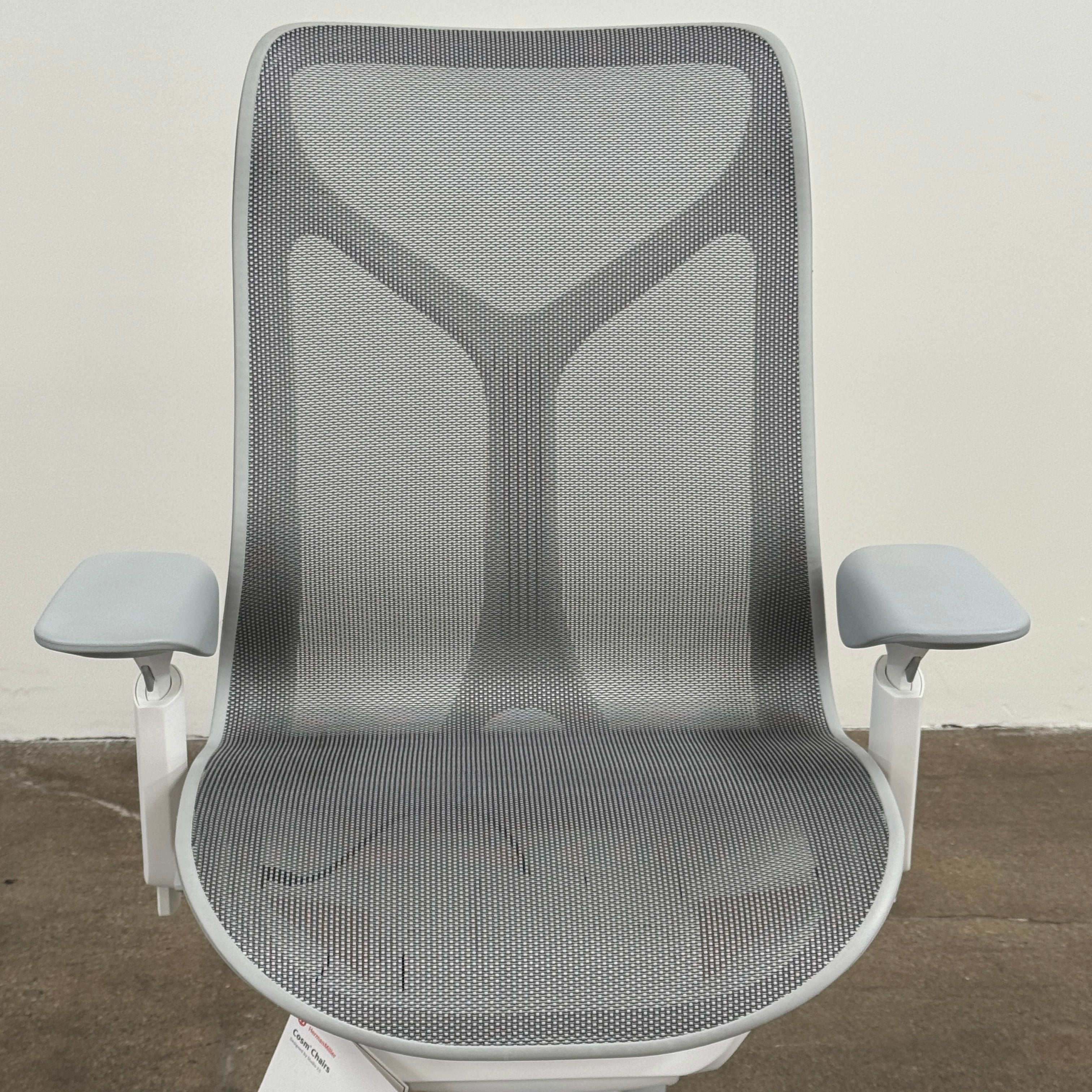 A sleek, modern white Herman Miller Cosm Office Chair featuring a mesh back and seat, supportive armrests, and five caster wheels is showcased on a concrete floor against an off-white wall. Designed by Herman Miller, this ergonomic chair seamlessly combines contemporary style with exceptional comfort.