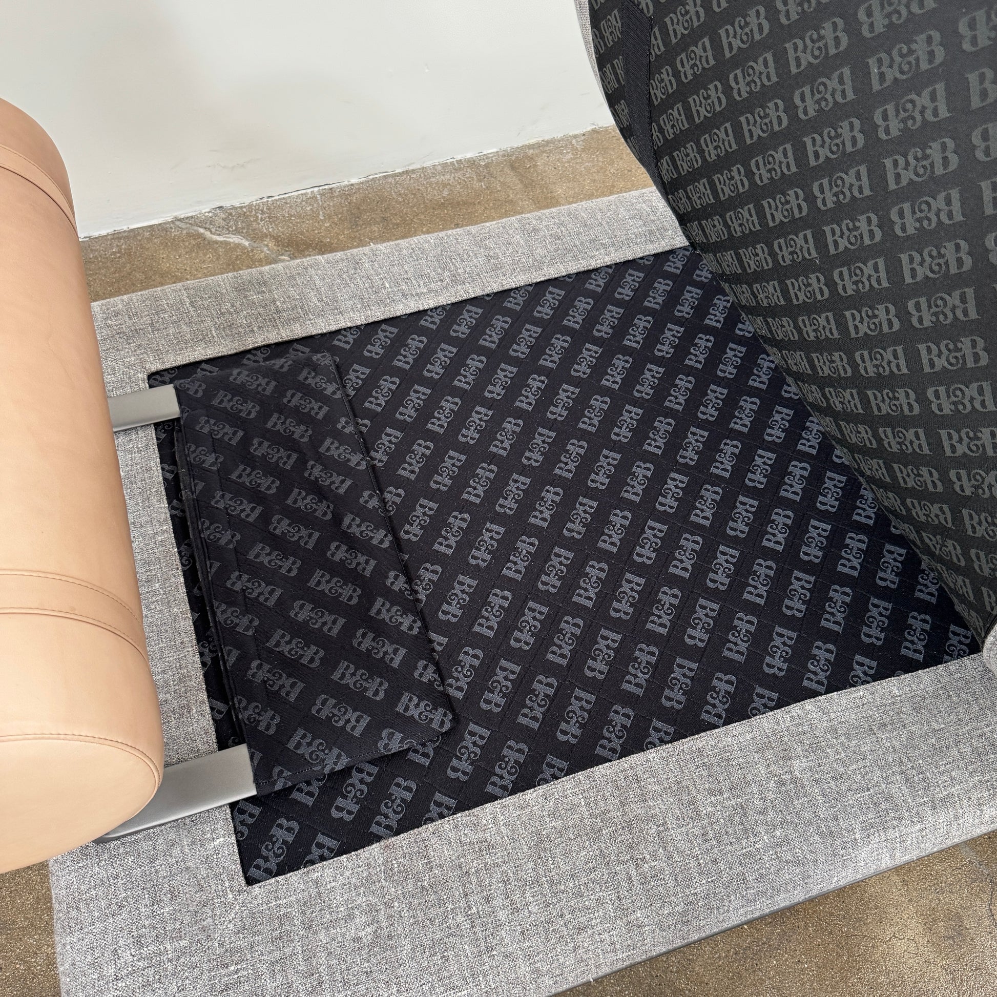 The B&B Italia Atoll Bench with Leather Bolsters by B&B Italia is a modern gray upholstered daybed featuring two cylindrical tan leather bolsters at each end, set on a sleek black metal frame and shown against a white background.