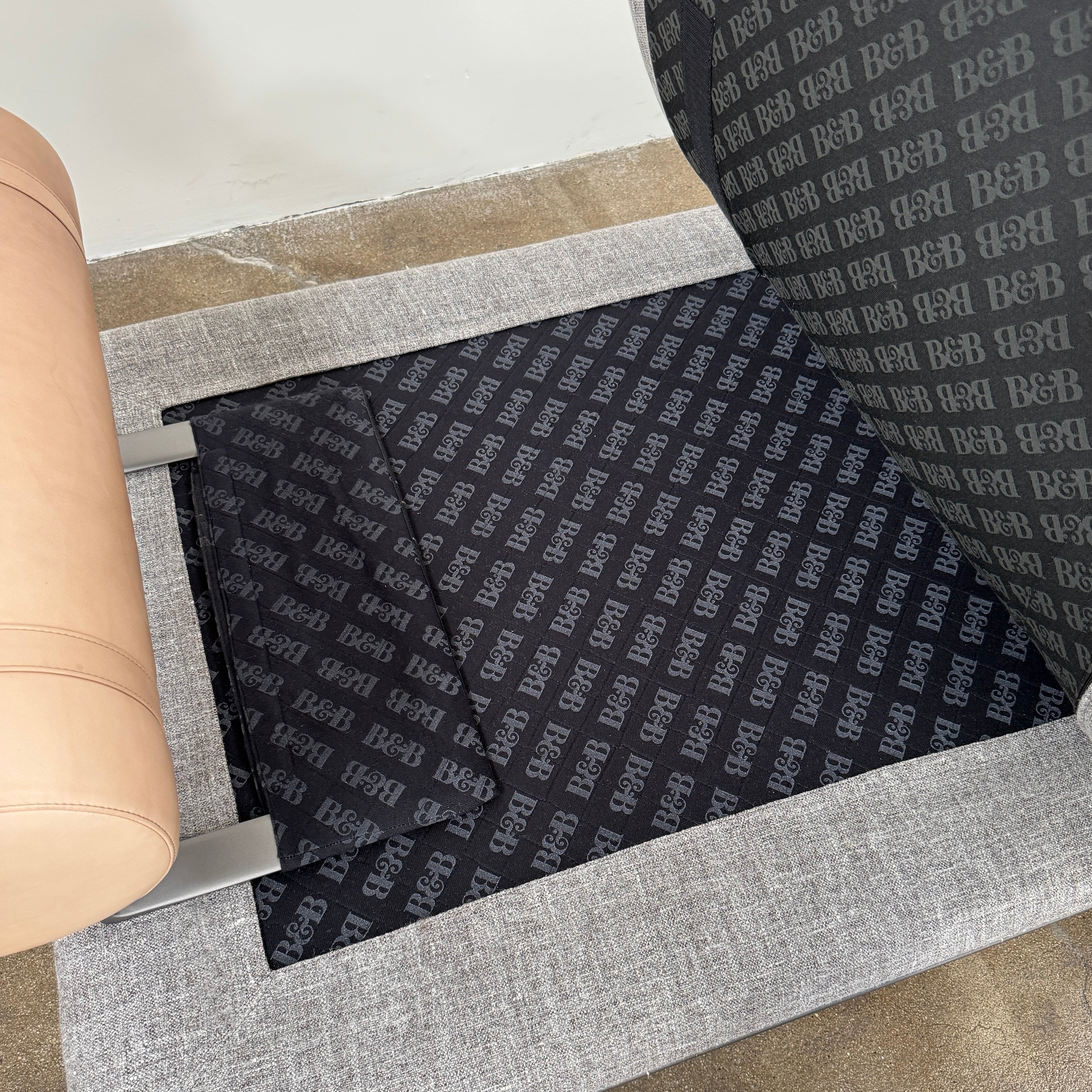 The B&B Italia Atoll Bench with Leather Bolsters by B&B Italia is a modern gray upholstered daybed featuring two cylindrical tan leather bolsters at each end, set on a sleek black metal frame and shown against a white background.