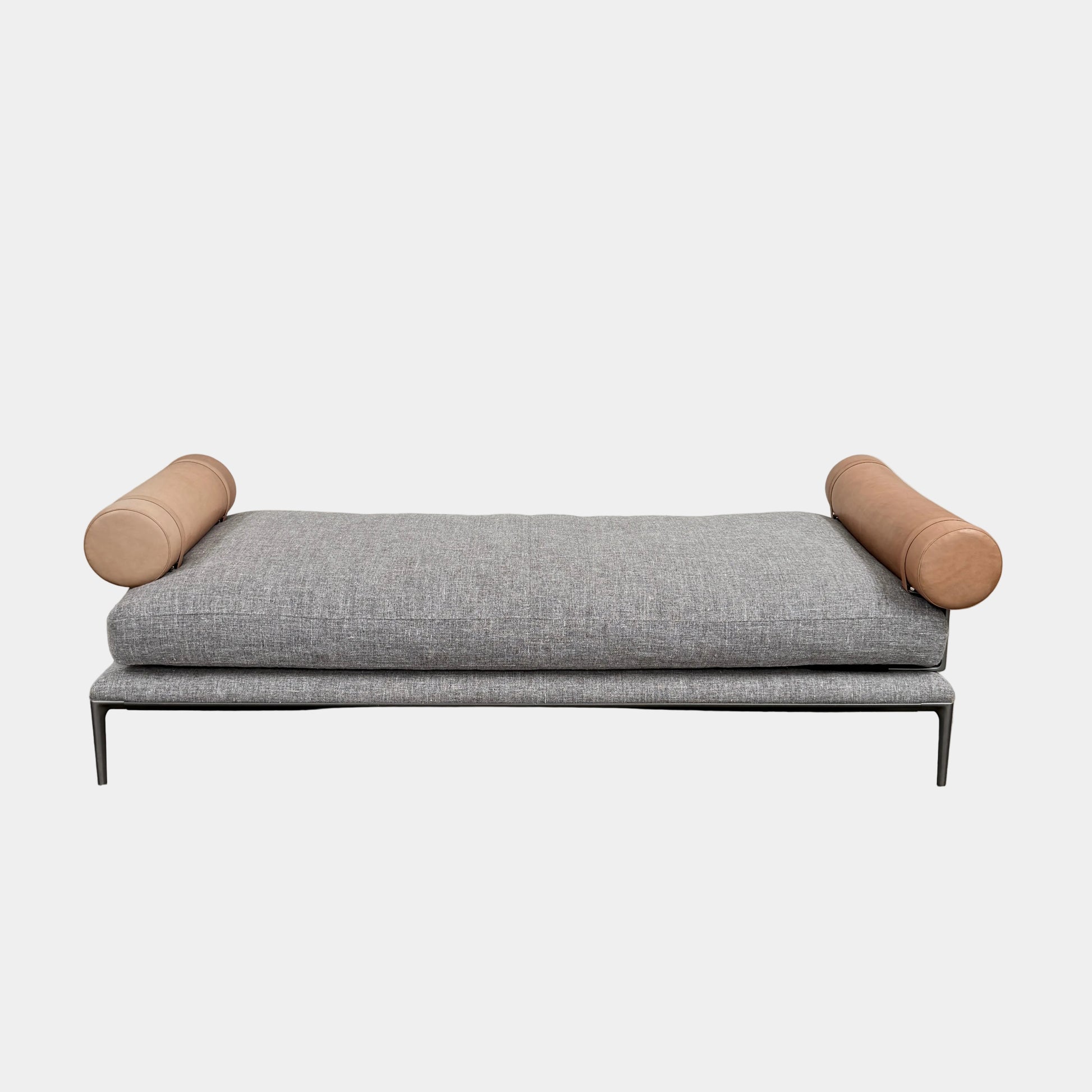 The B&B Italia Atoll Bench with Leather Bolsters by B&B Italia is a modern gray upholstered daybed featuring two cylindrical tan leather bolsters at each end, set on a sleek black metal frame and shown against a white background.