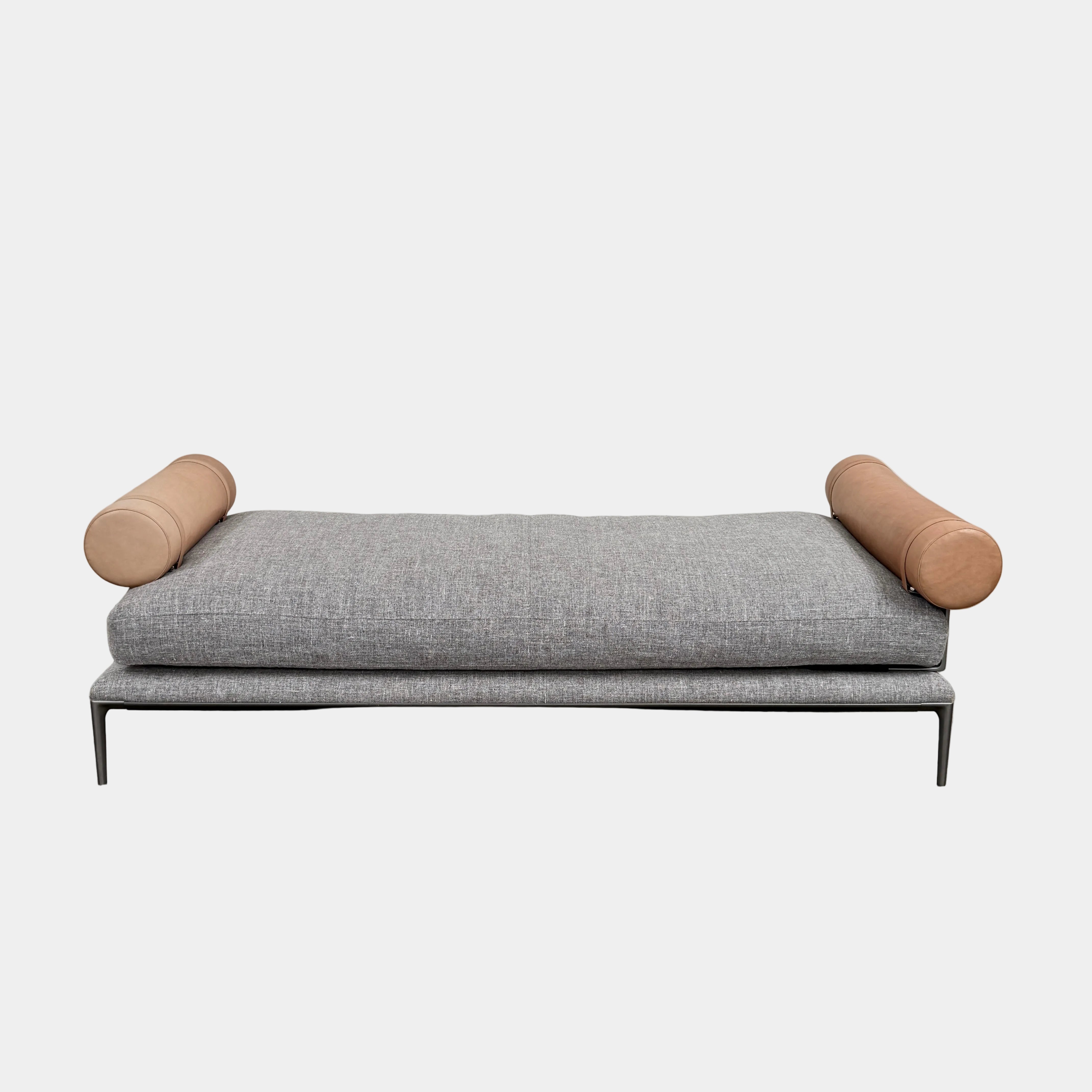 The B&B Italia Atoll Bench with Leather Bolsters by B&B Italia is a modern gray upholstered daybed featuring two cylindrical tan leather bolsters at each end, set on a sleek black metal frame and shown against a white background.