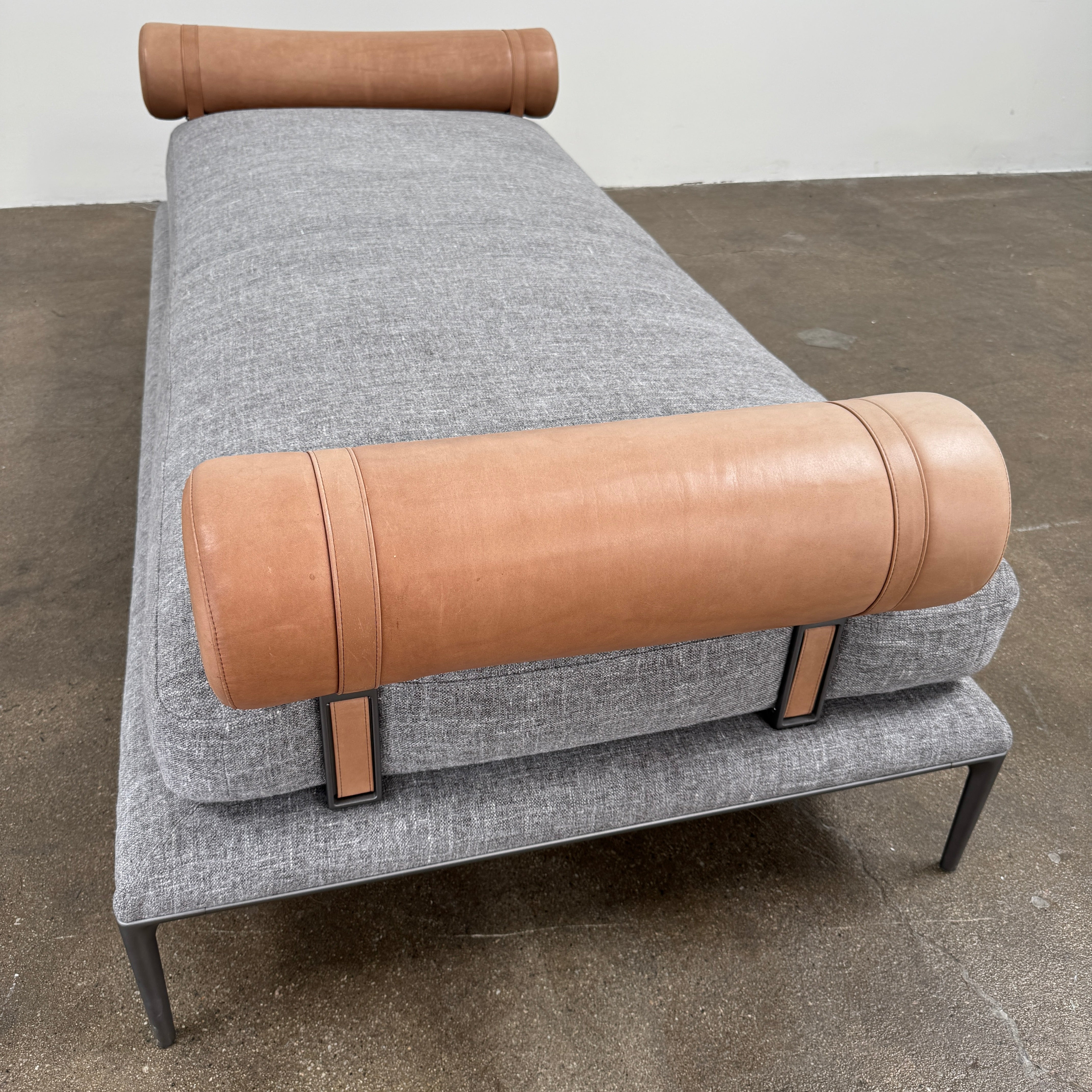 The B&B Italia Atoll Bench with Leather Bolsters by B&B Italia is a modern gray upholstered daybed featuring two cylindrical tan leather bolsters at each end, set on a sleek black metal frame and shown against a white background.