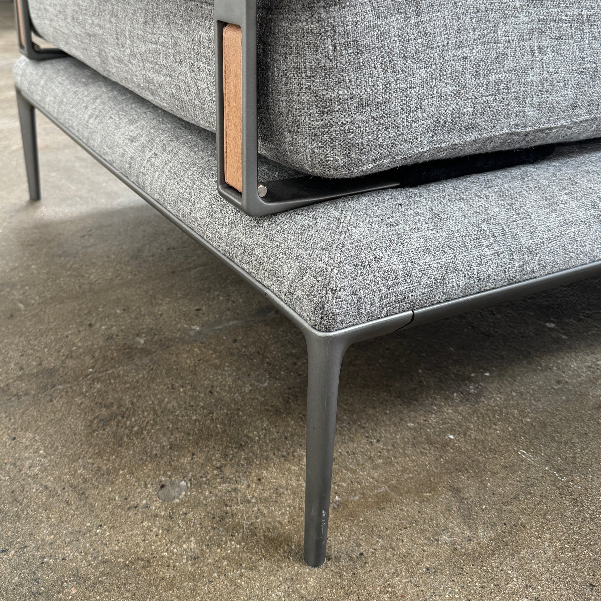 The B&B Italia Atoll Bench with Leather Bolsters by B&B Italia is a modern gray upholstered daybed featuring two cylindrical tan leather bolsters at each end, set on a sleek black metal frame and shown against a white background.