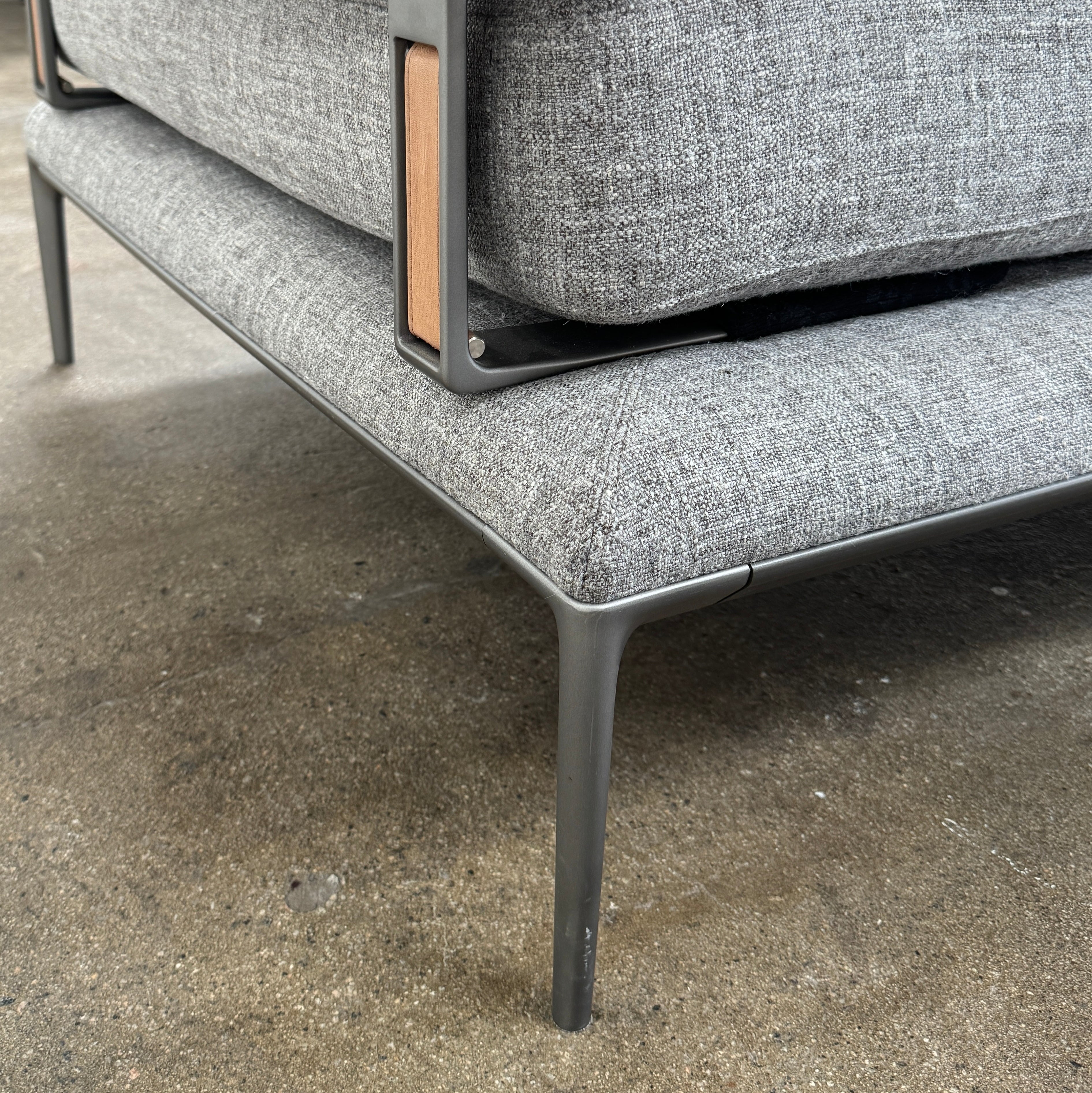 The B&B Italia Atoll Bench with Leather Bolsters by B&B Italia is a modern gray upholstered daybed featuring two cylindrical tan leather bolsters at each end, set on a sleek black metal frame and shown against a white background.